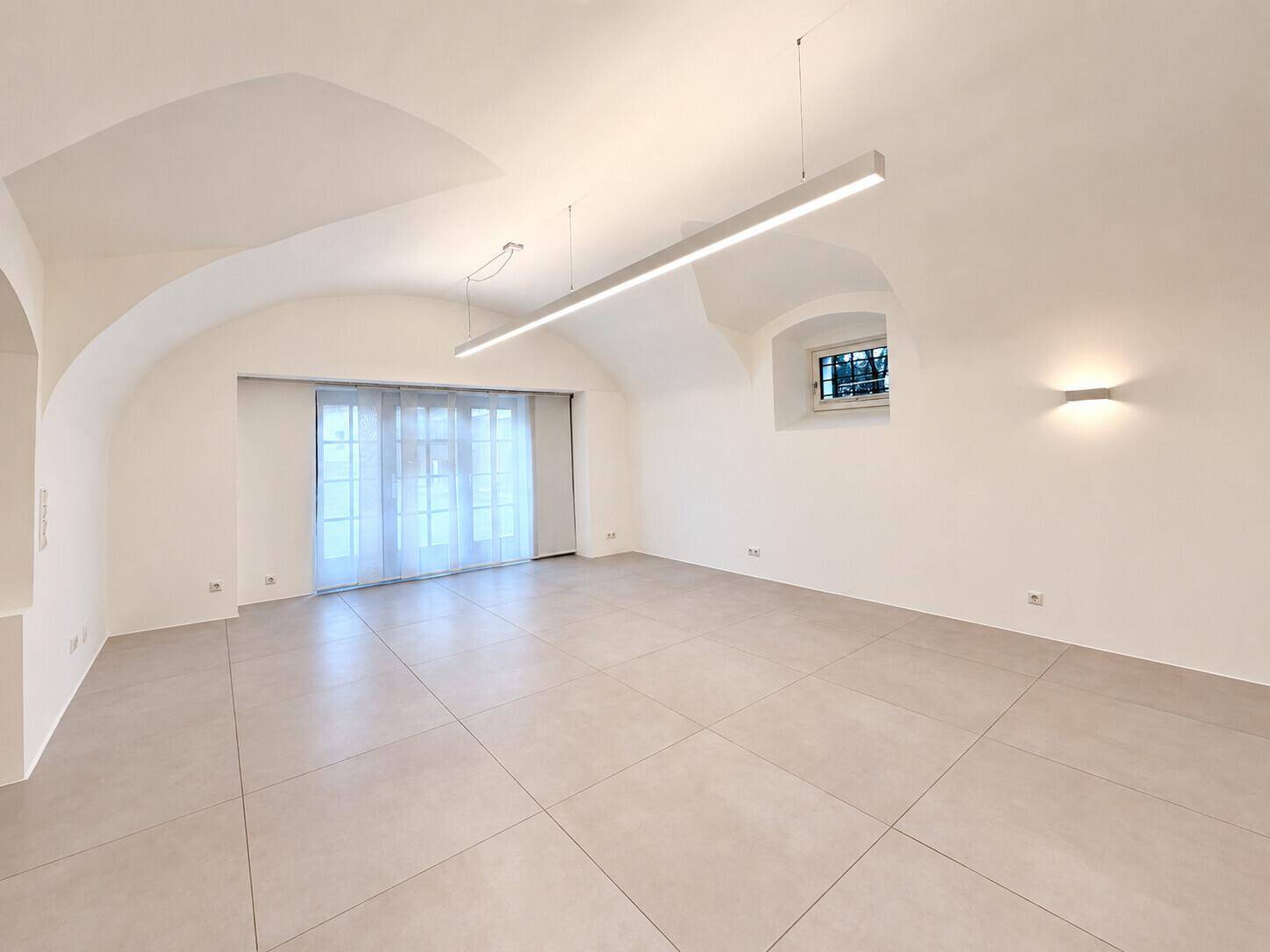 Weitläufiger Wohnbereich mit eleganten Gewölbedecken, modernen Lichtleisten und hellem Fliesenboden.