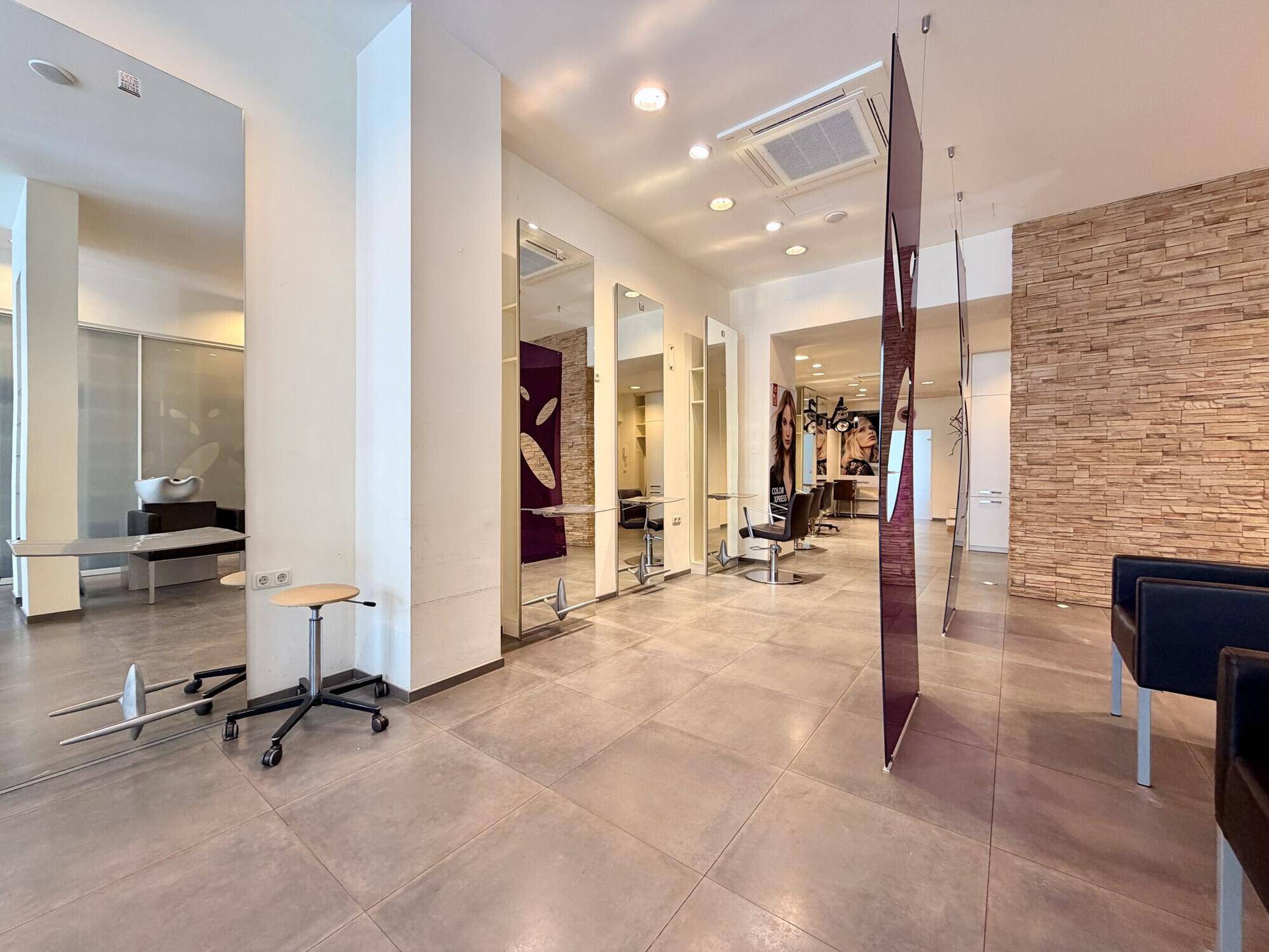 Moderner Friseursalon mit großen Spiegeln, Steinwandakzent und grauen Fliesen.