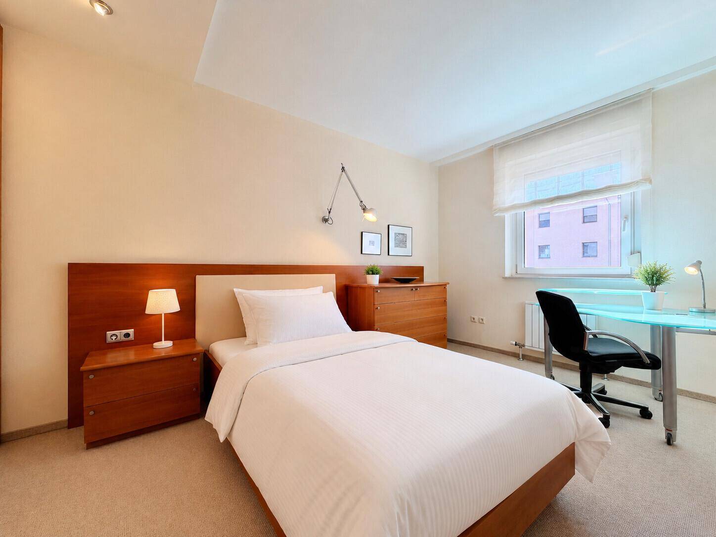 Helles Schlafzimmer mit Einzelbett, Schreibtisch und Teppichboden, ideal als Gäste- oder Kinderzimmer.