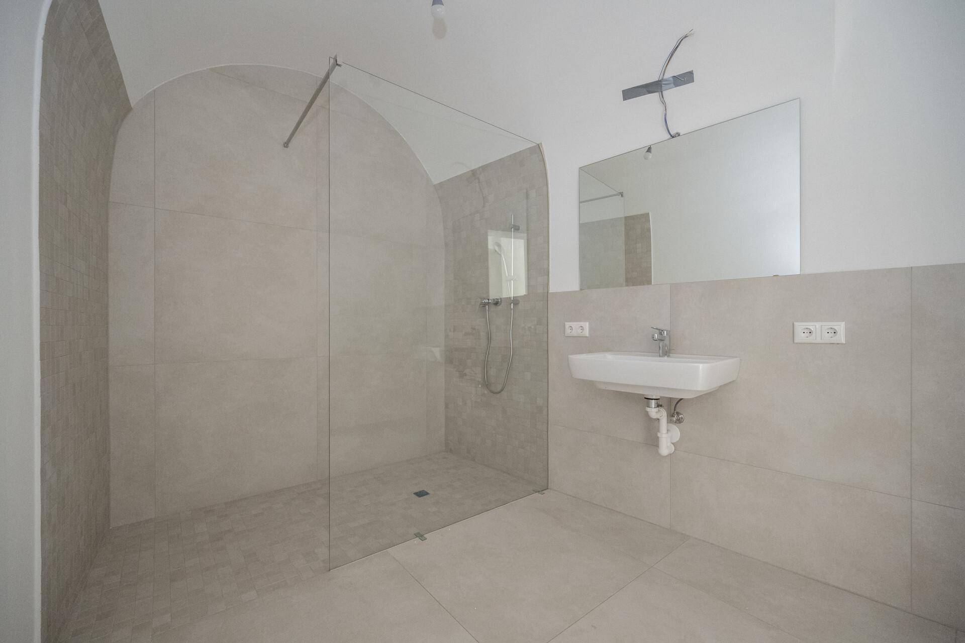 Geräumiges Badezimmer mit großer begehbarer Dusche, Fliesenboden und modernem Waschbecken.