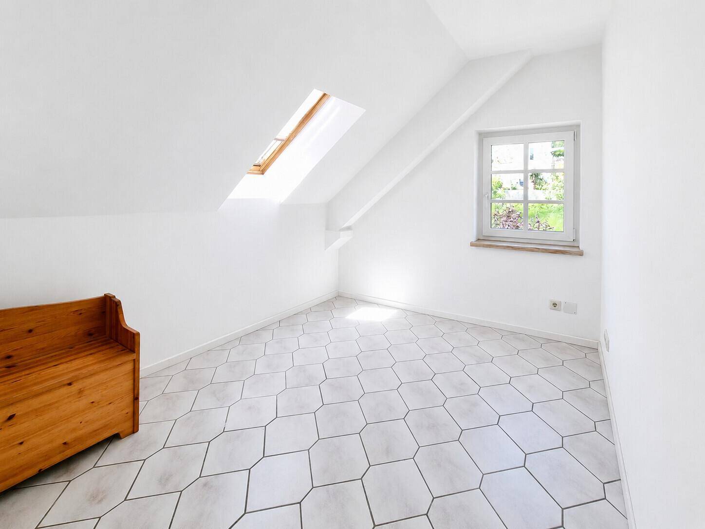 Helles Zimmer im Dachgeschoss mit Fliesenboden, Dachfenster und Gartenblick.