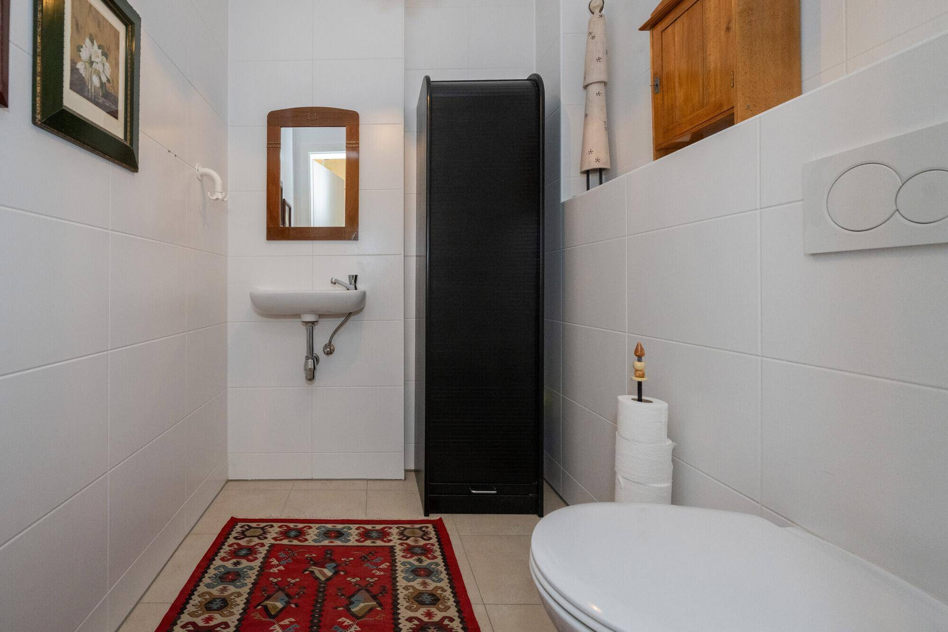 Kleines Gäste-WC mit weißen Fliesen, Waschbecken und Wand-WC.