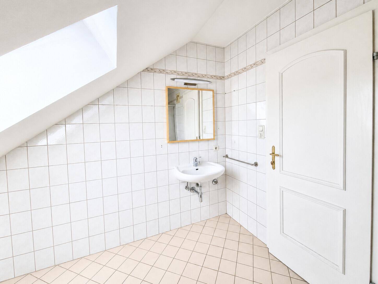 Badezimmer im Dachgeschoss mit Fliesen, Waschbecken und Spiegelschrank.