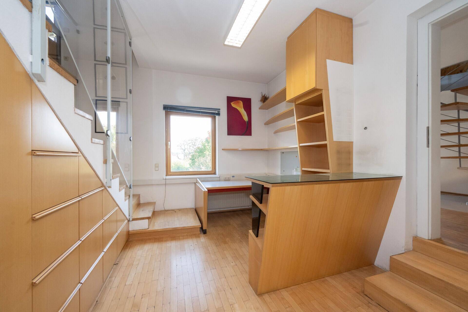 Kompaktes Büro mit Holzparkett, integriertem Schreibtisch und Stauraum unter der Treppe.