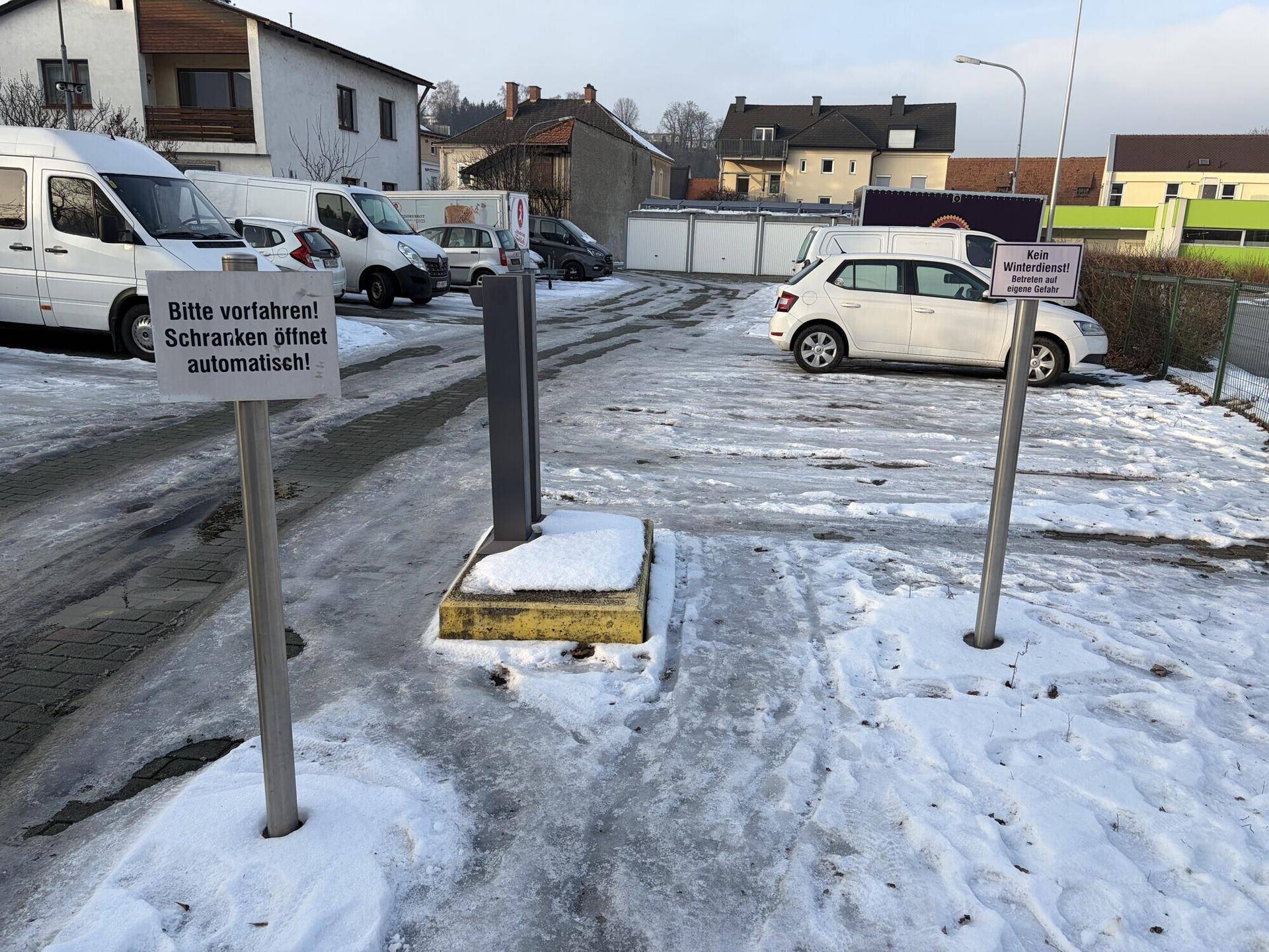 Ausgangsbereich eines Parkplatzes mit Hinweisschildern zur Schrankenöffnung und Schnee auf dem Boden.