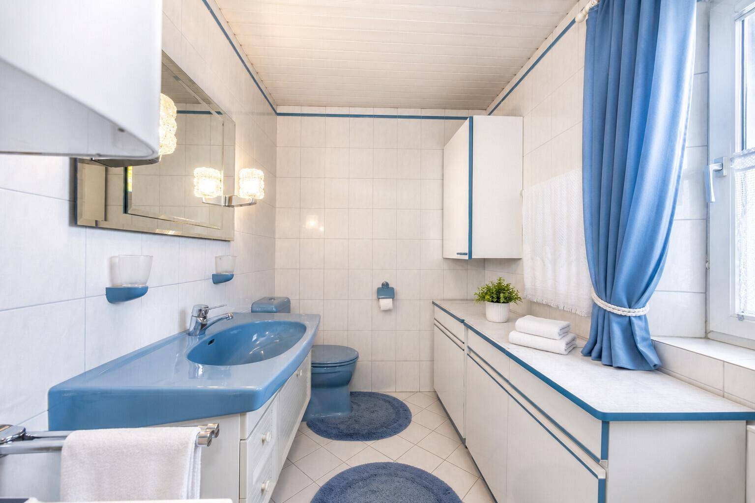 Badezimmer im 80er-Jahre-Stil mit blauen Akzenten, Fliesen und Fenster.