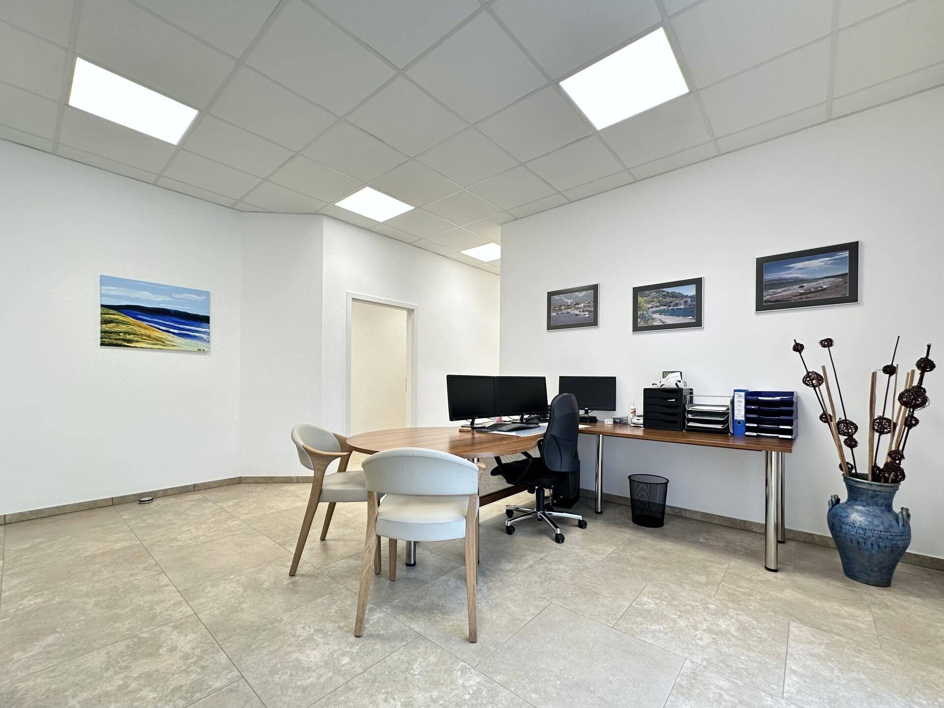 Modernes Büro mit einem großen Schreibtisch, zwei Monitoren und einem hellen Fliesenboden.