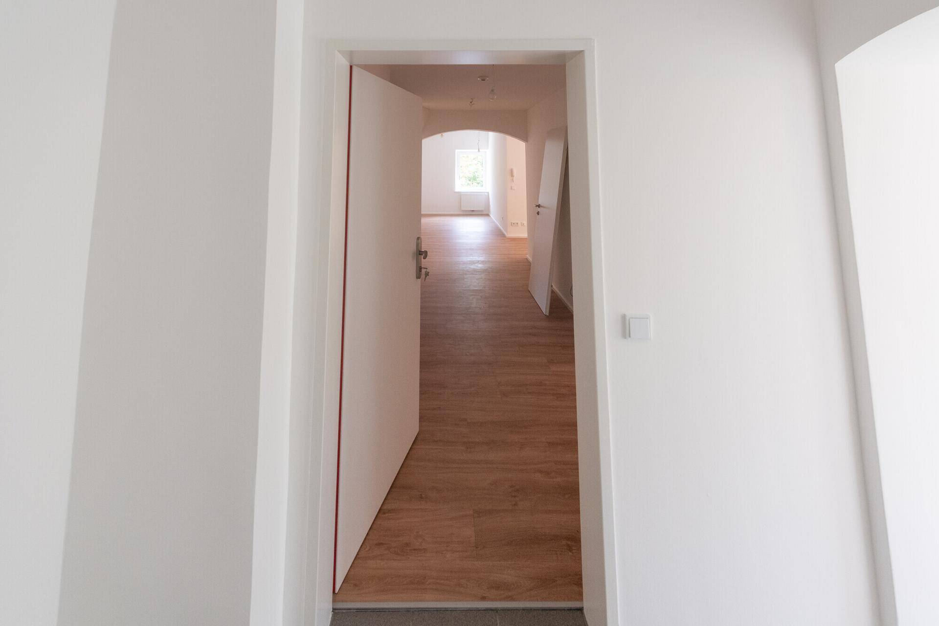 Heller Eingangsbereich mit Laminatboden und offener Tür, die den Blick in weitere Räume freigibt.