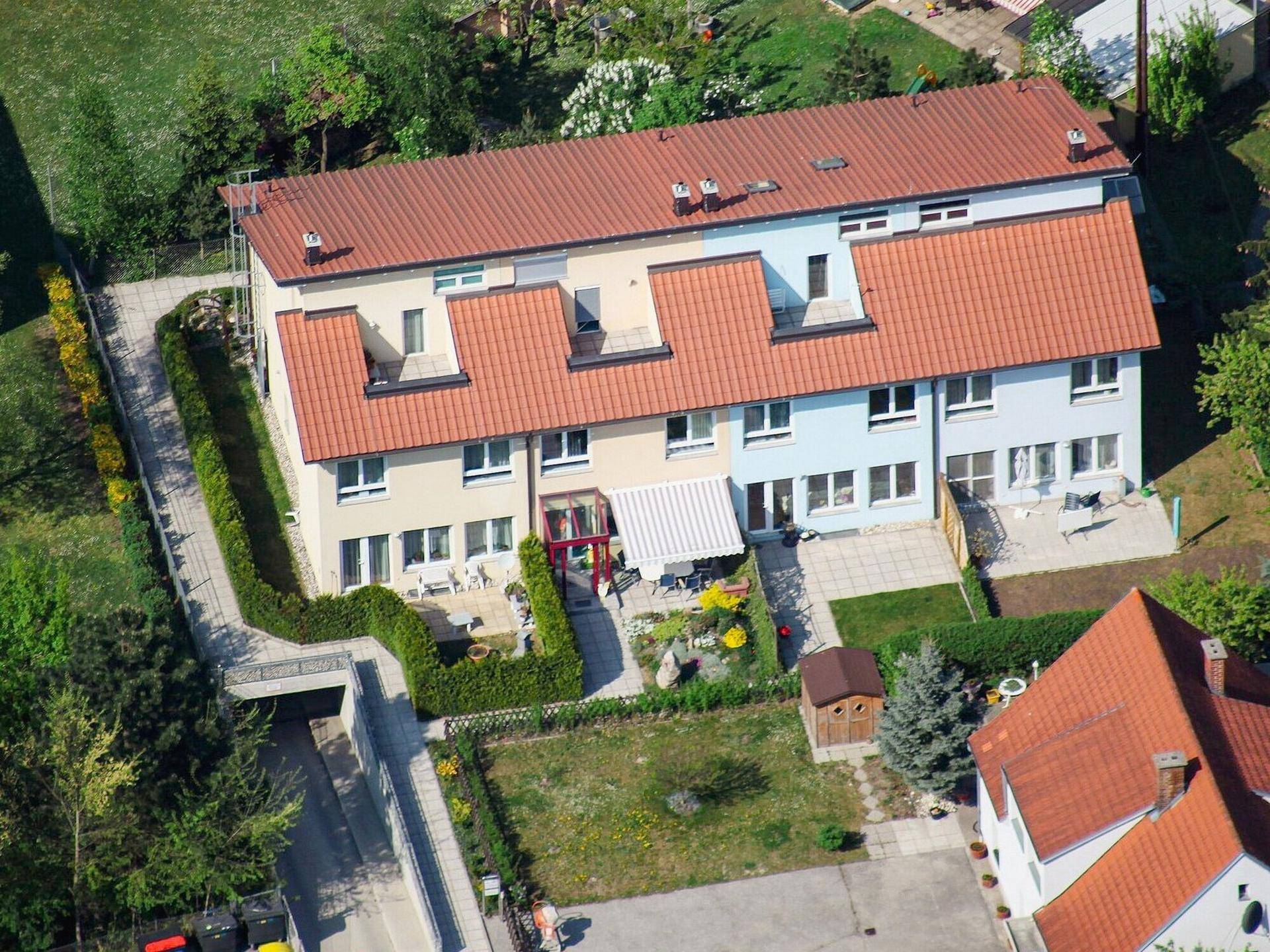 Luftaufnahme einer Reihe von Reihenhäusern mit roten Ziegeldächern und privaten Gärten.