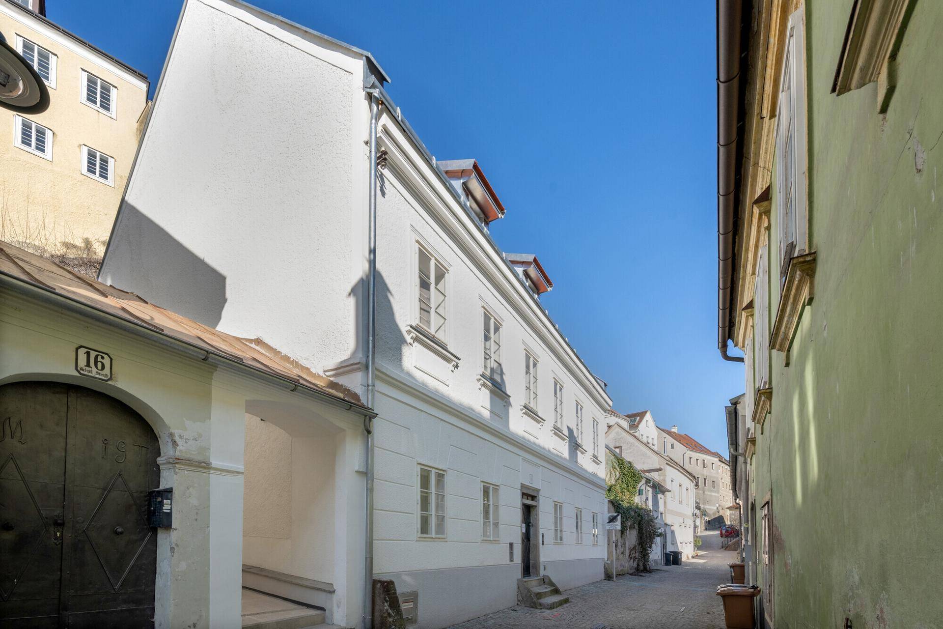 Historisches Gebäude in einer engen Gasse mit traditioneller Architektur und weißer Fassade unter blauem Himmel.