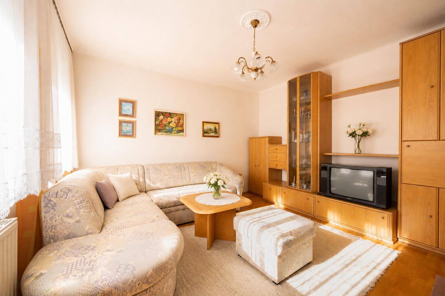 Gemütliches Wohnzimmer mit Ecksofa, Teppichboden und Holzmöbeln in warmen Farbtönen.