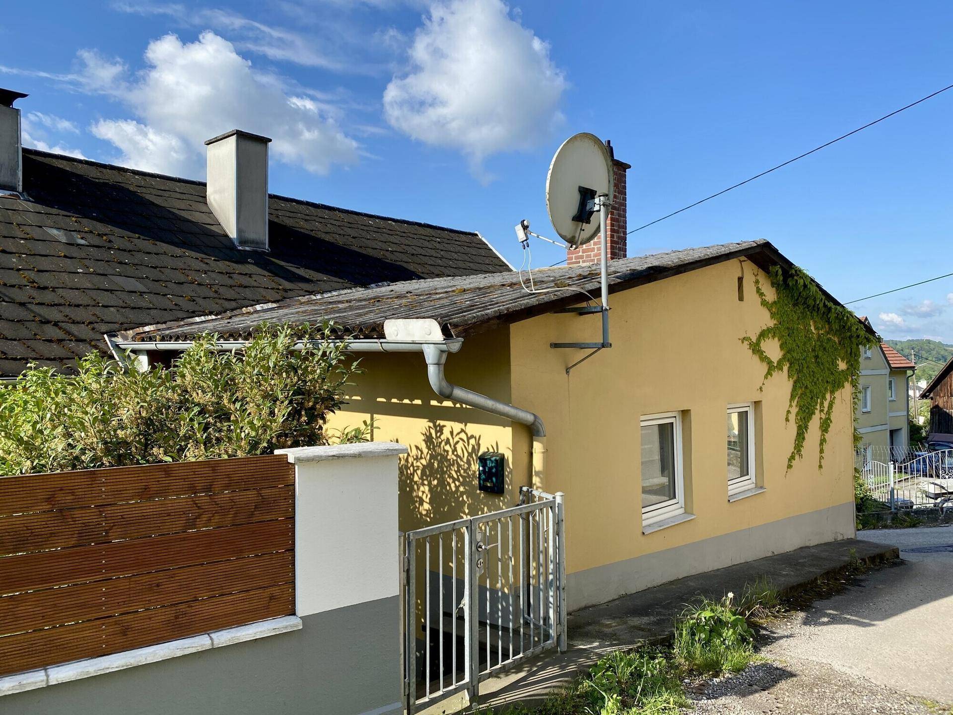 Seitenansicht des Hauses mit Satellitenschüssel, Dach und umzäuntem Bereich.
