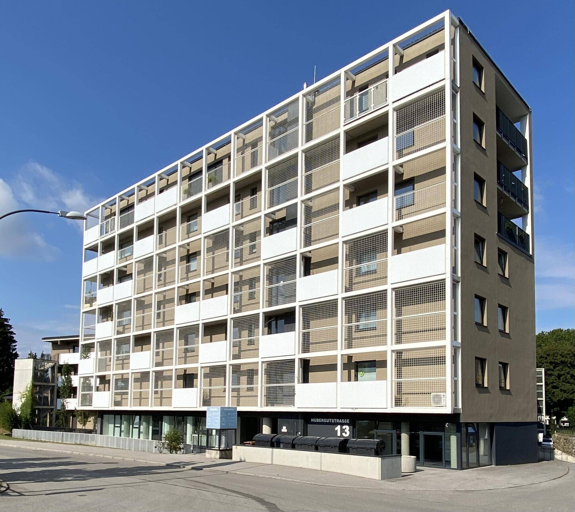 Zeitgenössisches Wohngebäude mit Balkonen und einer hellen Fassade unter blauem Himmel.
