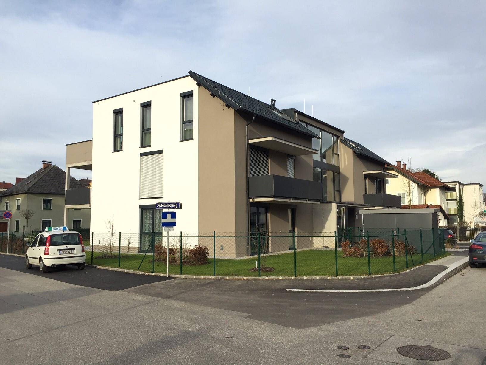 Modernes Mehrfamilienhaus mit heller Fassade und Balkonen an einer Straßenecke.
