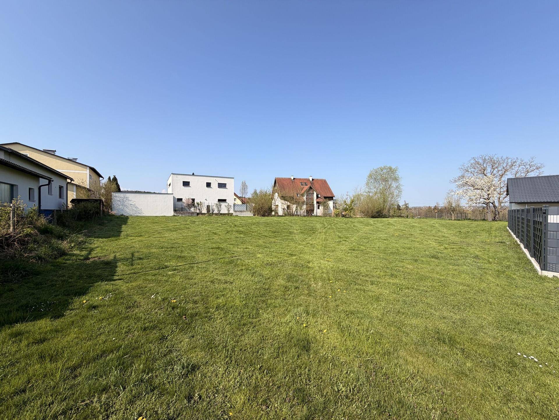 Großes grünes Grundstück mit verschiedenen Wohnhäusern in der Umgebung unter blauem Himmel.