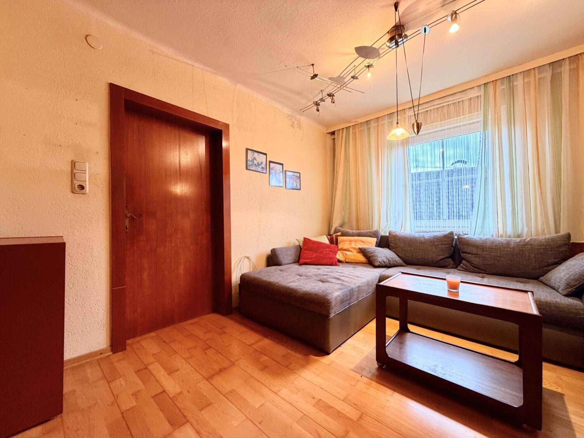Gemütliches Wohnzimmer mit großem Sofa, Holzboden und Fenster mit Vorhängen.
