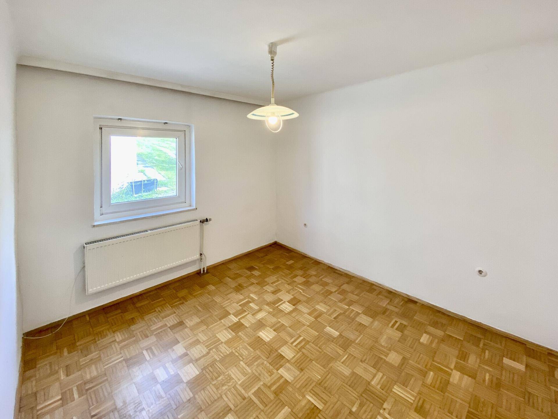 Leeres Zimmer mit Parkettboden, weiß gestrichenen Wänden und einem Fenster.