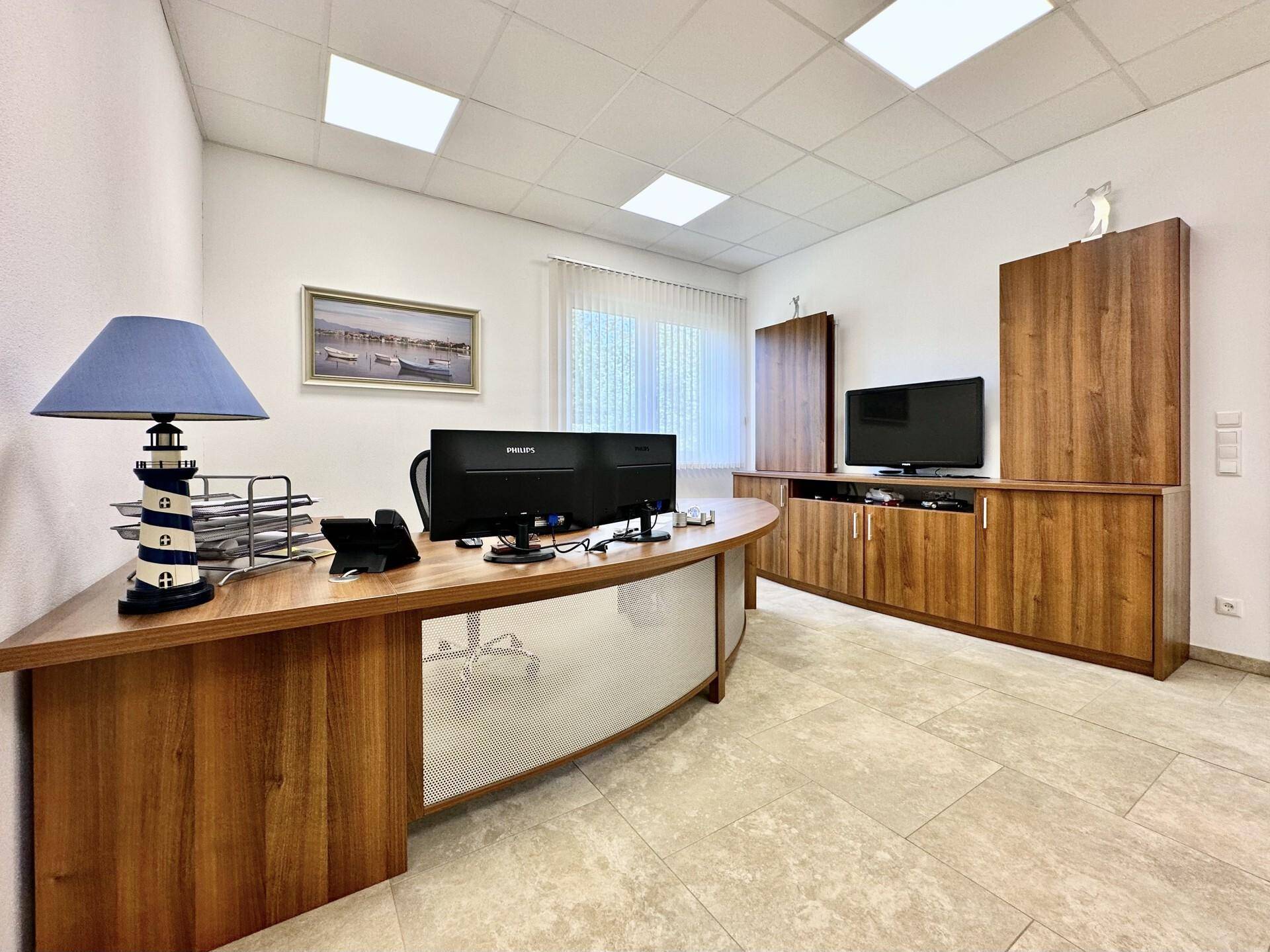 Geräumiges Büro mit einem geschwungenen Holzschreibtisch, Monitoren, einem Fernseher und Holzschränken.