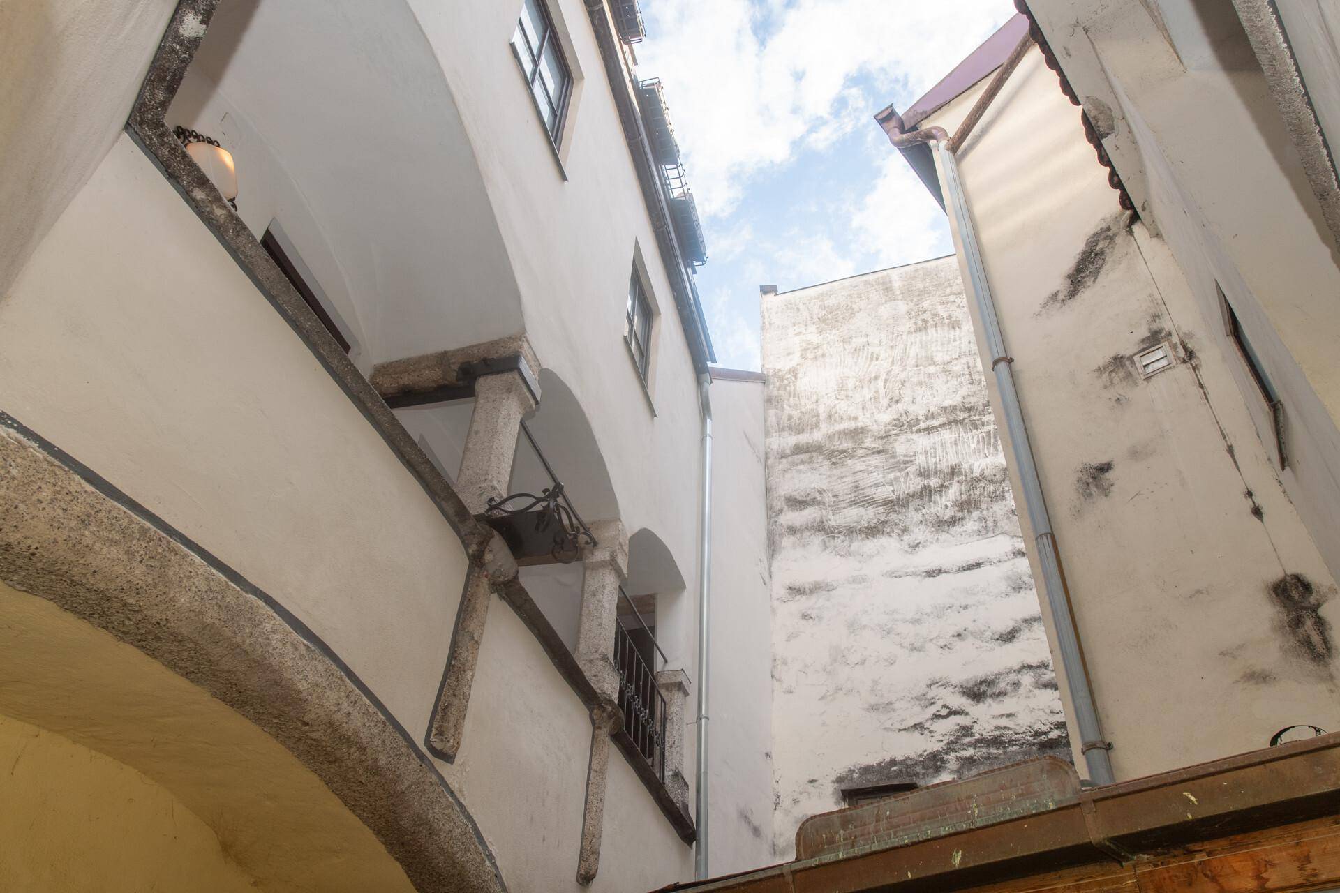 Blick nach oben in einen engen Innenhof mit historischen Gebäudefassaden und einem Stück Himmel.