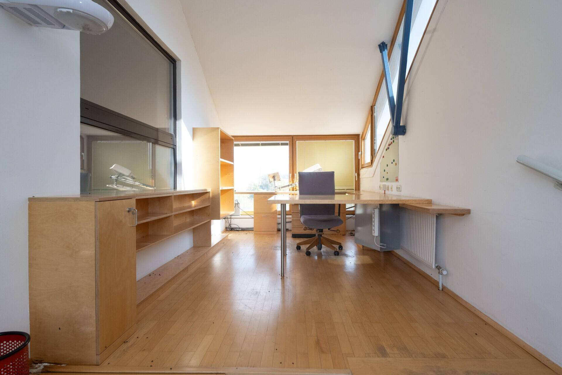 Büro mit Holzparkett, langen Arbeitsflächen und Regalen, ideal für kreatives Arbeiten.