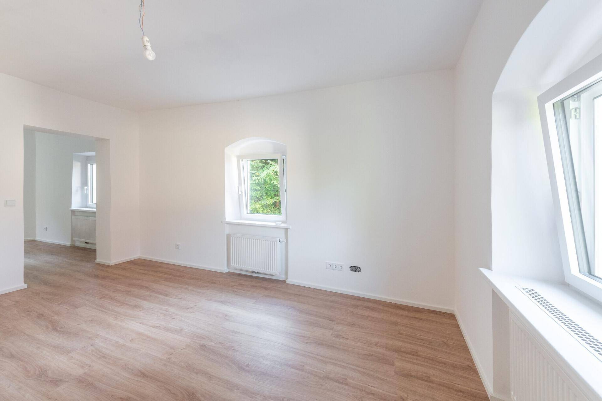 Heller, leerer Raum mit modernem Laminatboden und weißen Wänden, bereit zum Einzug.