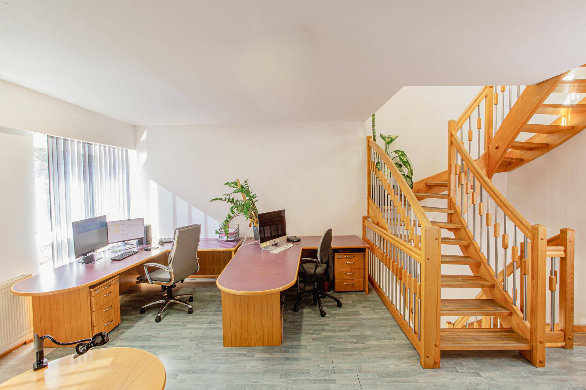 Offener Bürobereich mit mehreren Arbeitsplätzen und einer markanten, hellen Holztreppe.