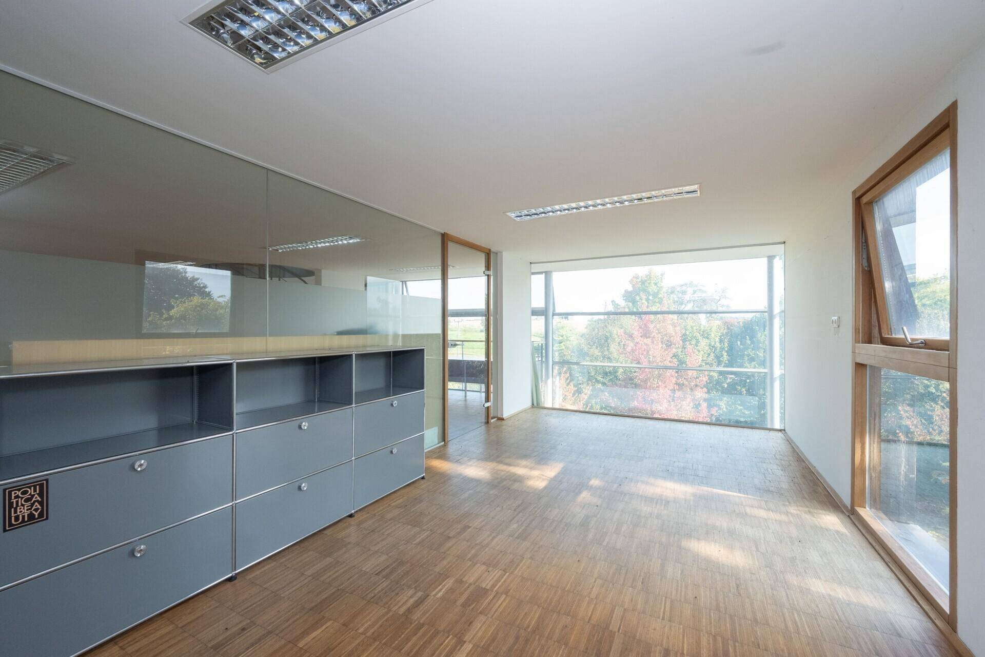 Modernes Büro mit großen Fenstern, Holzparkett und integrierten grauen Schränken.