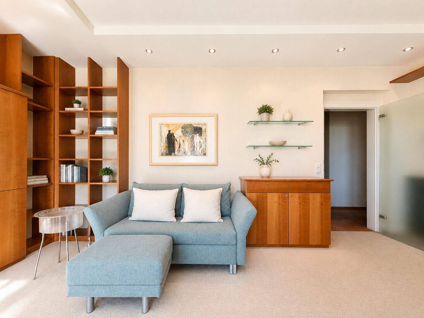 Gemütliches Wohnzimmer mit Sofa, Teppichboden und dekorativen Wandregalen aus Glas.