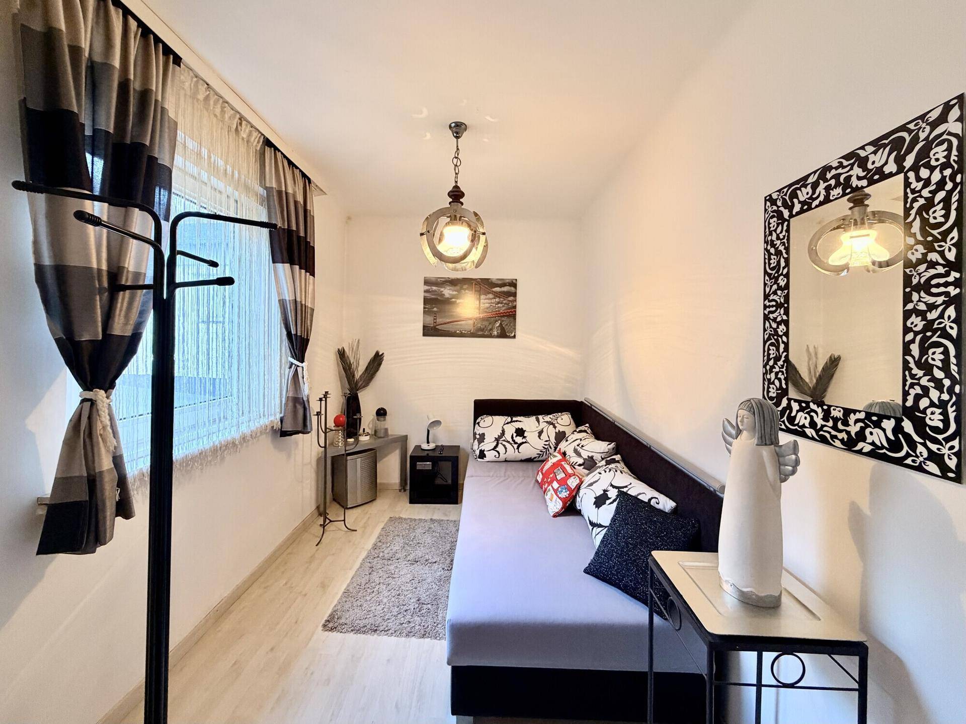 Helles Schlafzimmer mit Tagesbett, modernem Spiegel und minimalistischer Dekoration.