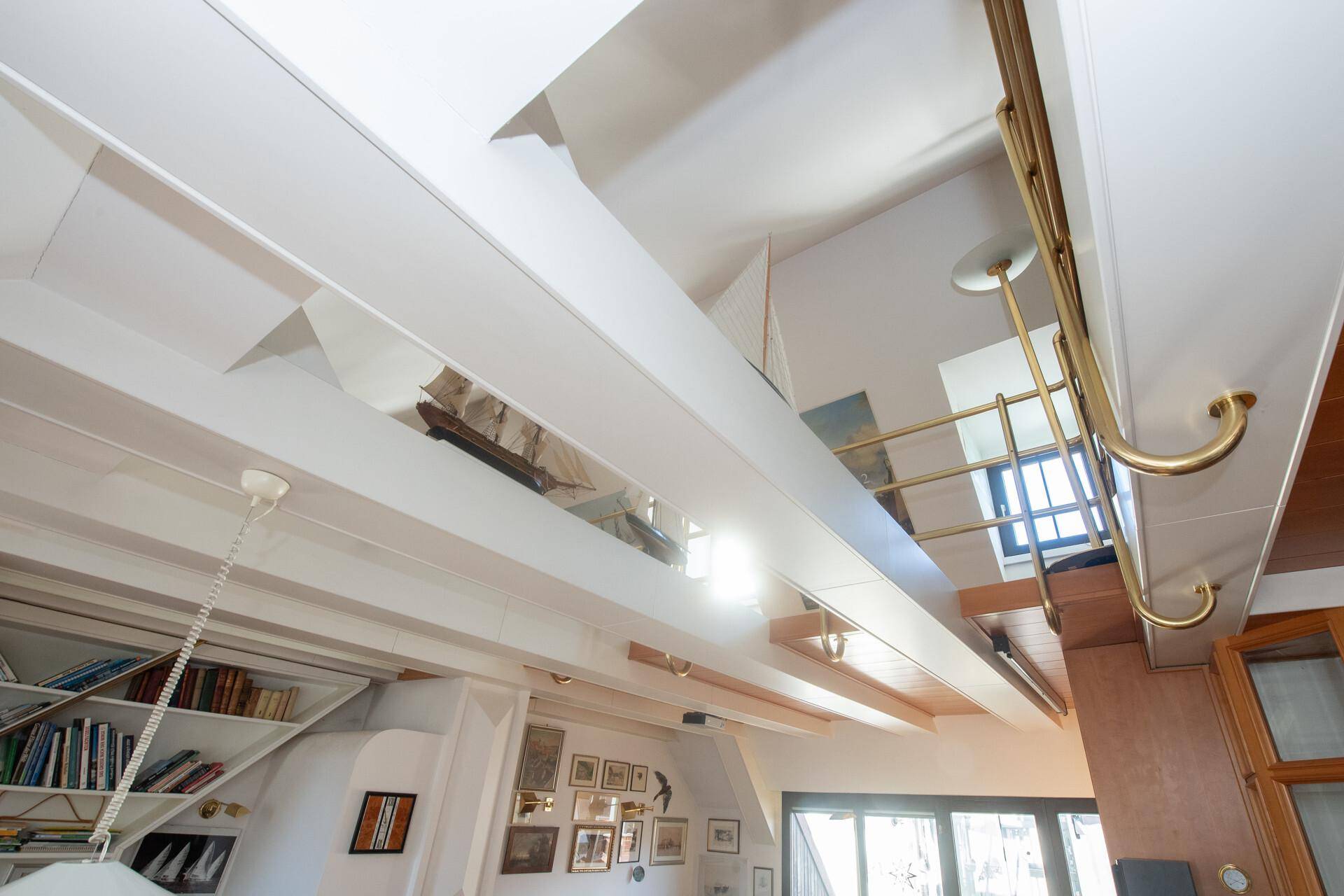 Blick von unten auf die offene Galerie über dem Wohnbereich mit Holzdecke und Messinggeländer.