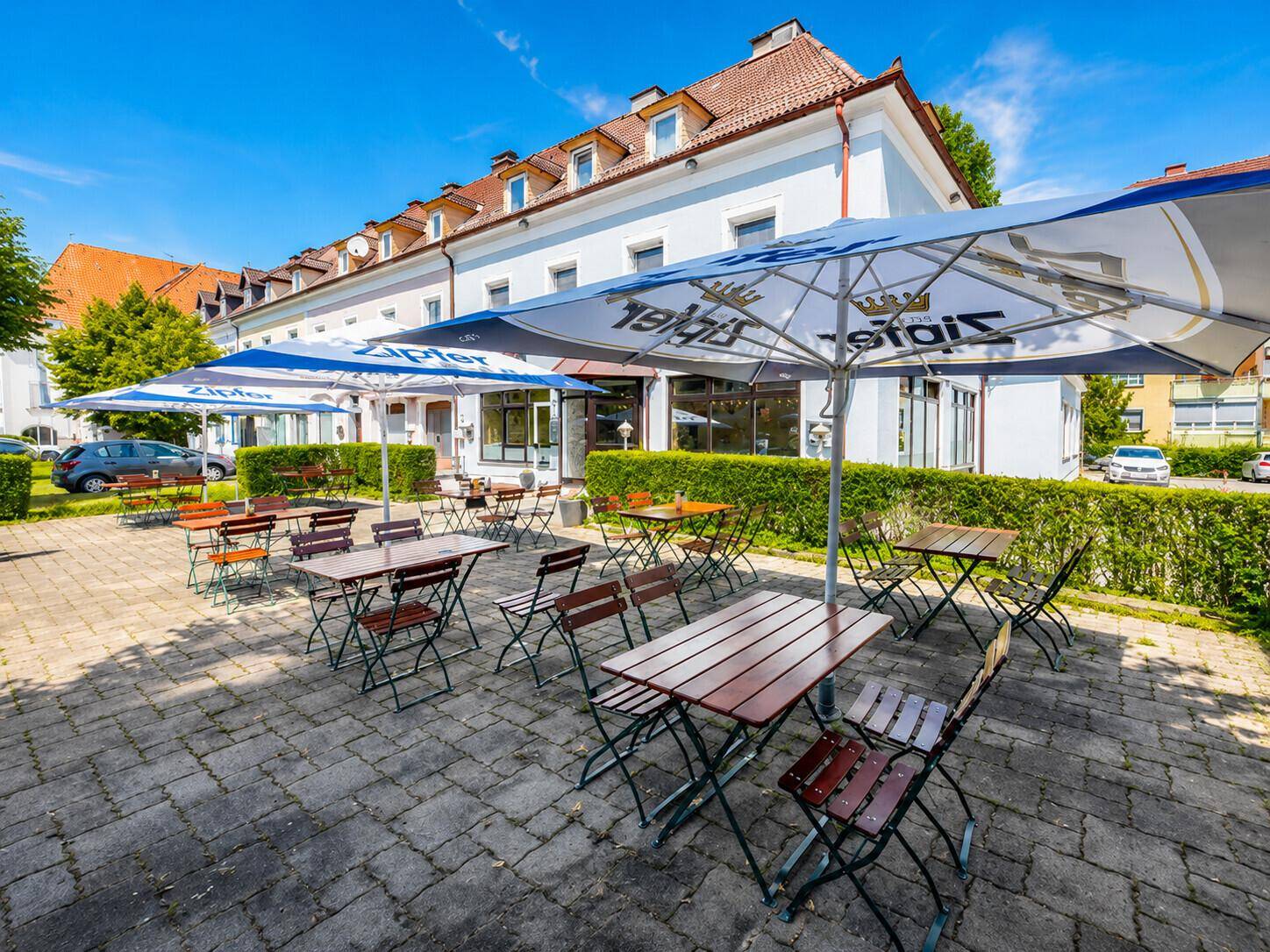 Weitläufige Außenterrasse mit zahlreichen Tischen und Stühlen unter großen Sonnenschirmen an einem sonnigen Tag.