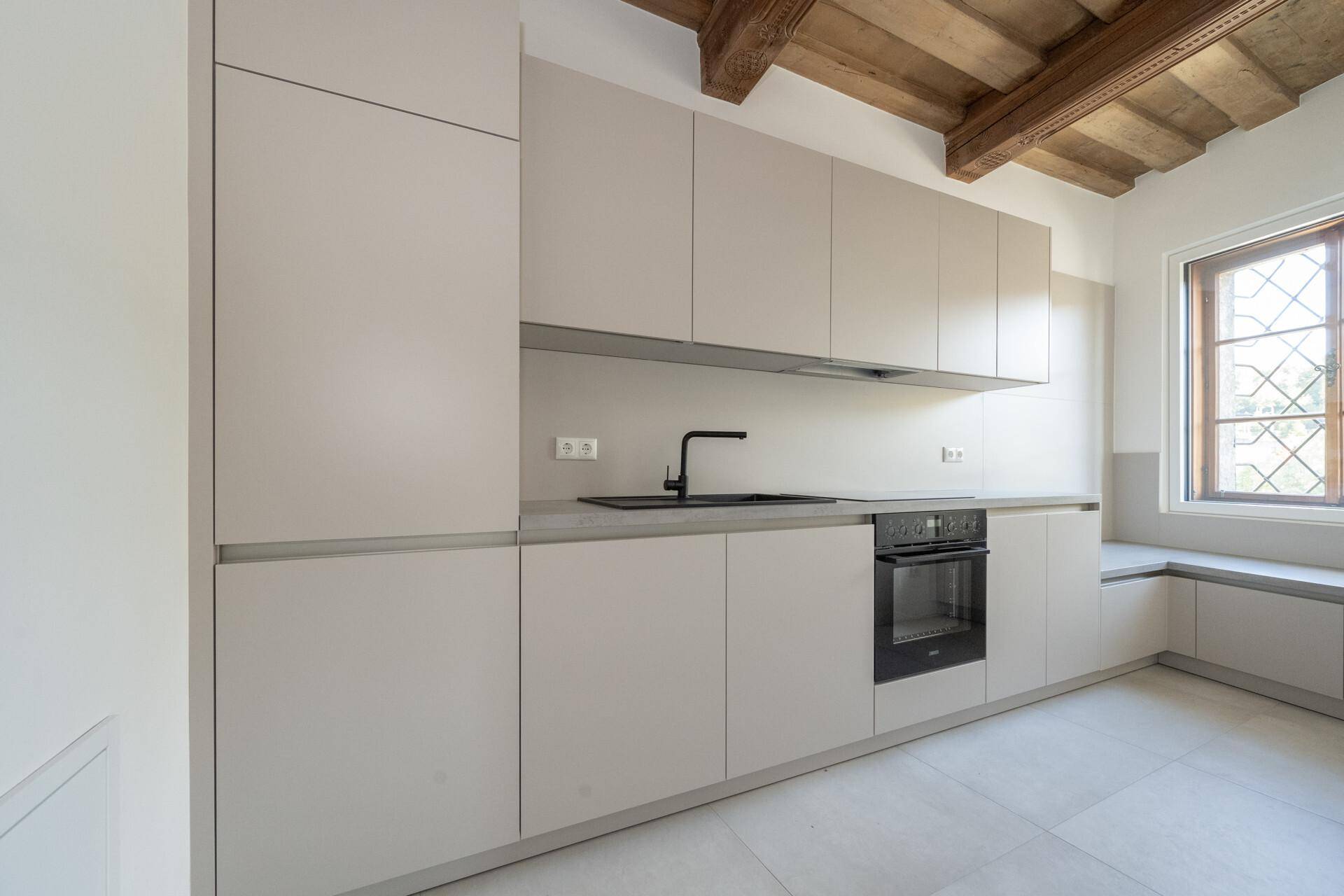 Helle, moderne Küche mit integrierten Geräten, grauen Schränken und einer gemütlichen Fensternische.