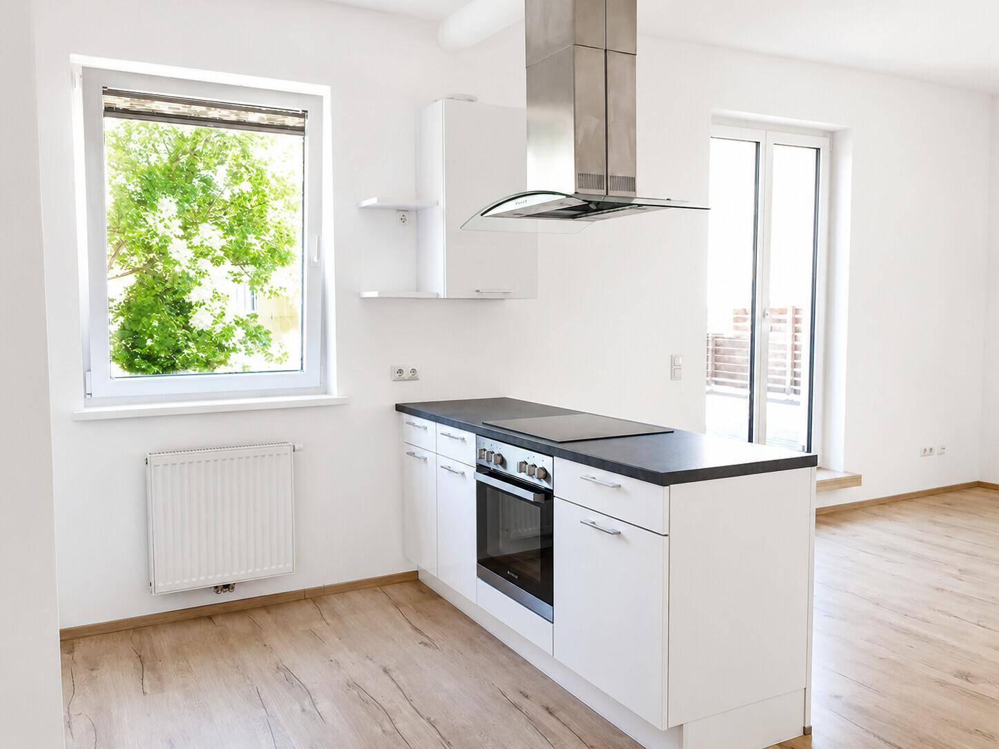 Helle, moderne Küche mit weißen Schränken, dunkler Arbeitsplatte und einem Fenster mit Blick ins Grüne.