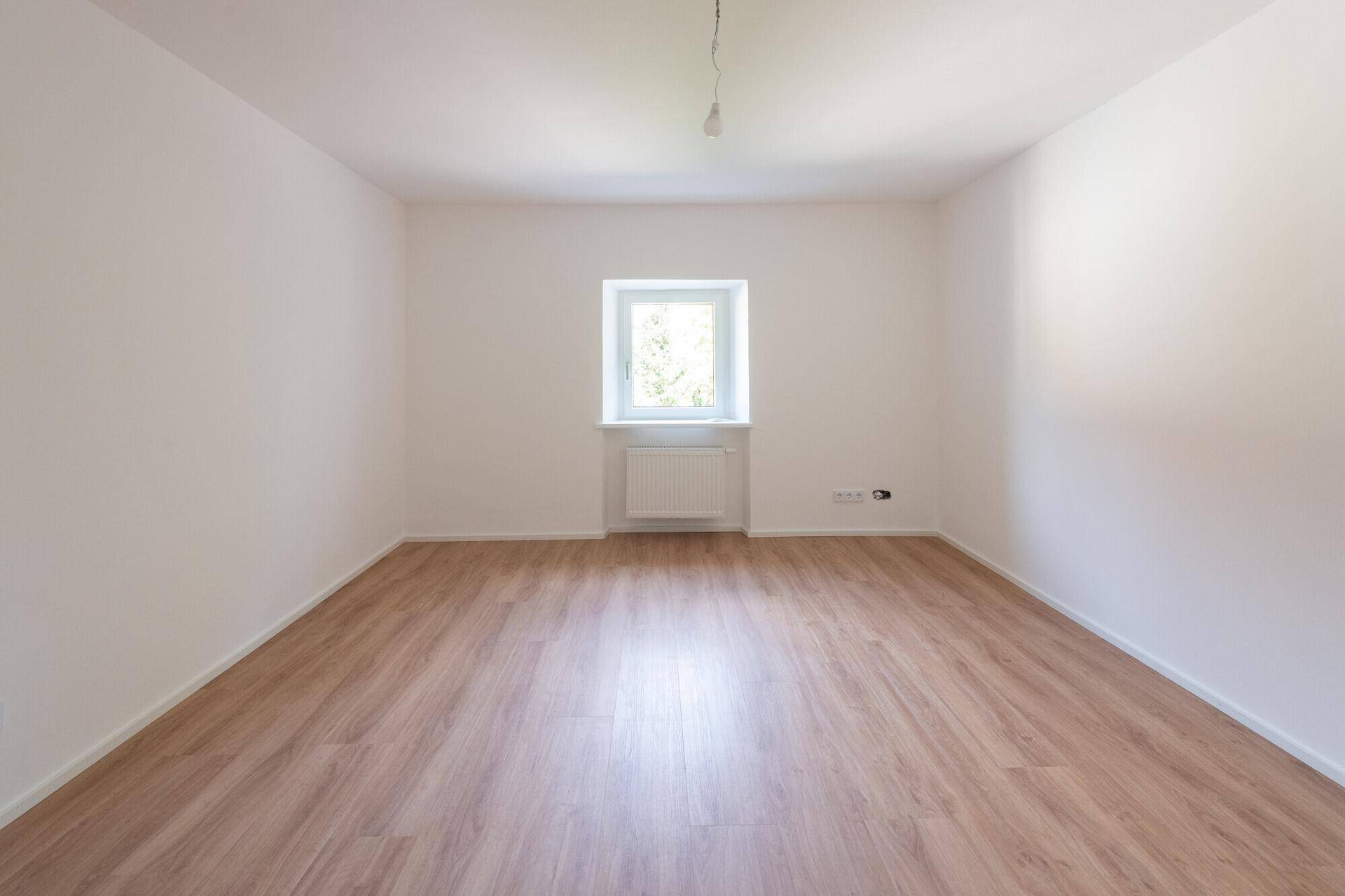 Ruhiges Schlafzimmer mit Laminatboden und einem Fenster, das viel Tageslicht hereinlässt.