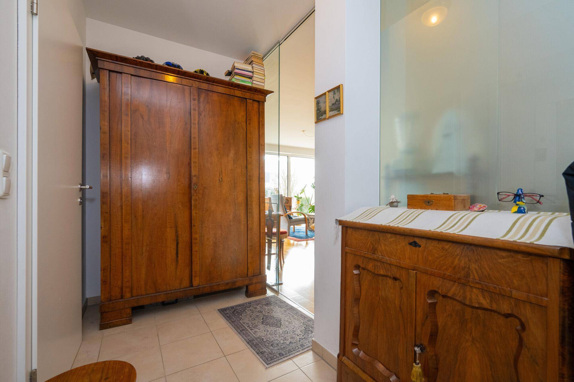 Eingangsbereich mit Fliesenboden und antiken Holzmöbeln, der in den Wohnbereich führt.