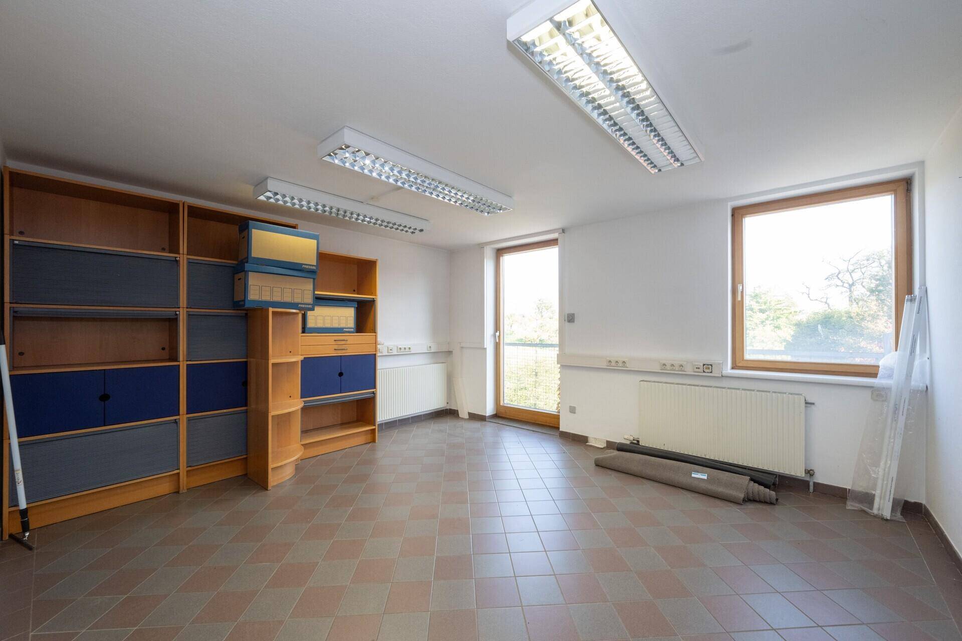 Helles Büro mit kariertem Fliesenboden, Regalen und Fensterblick ins Grüne.