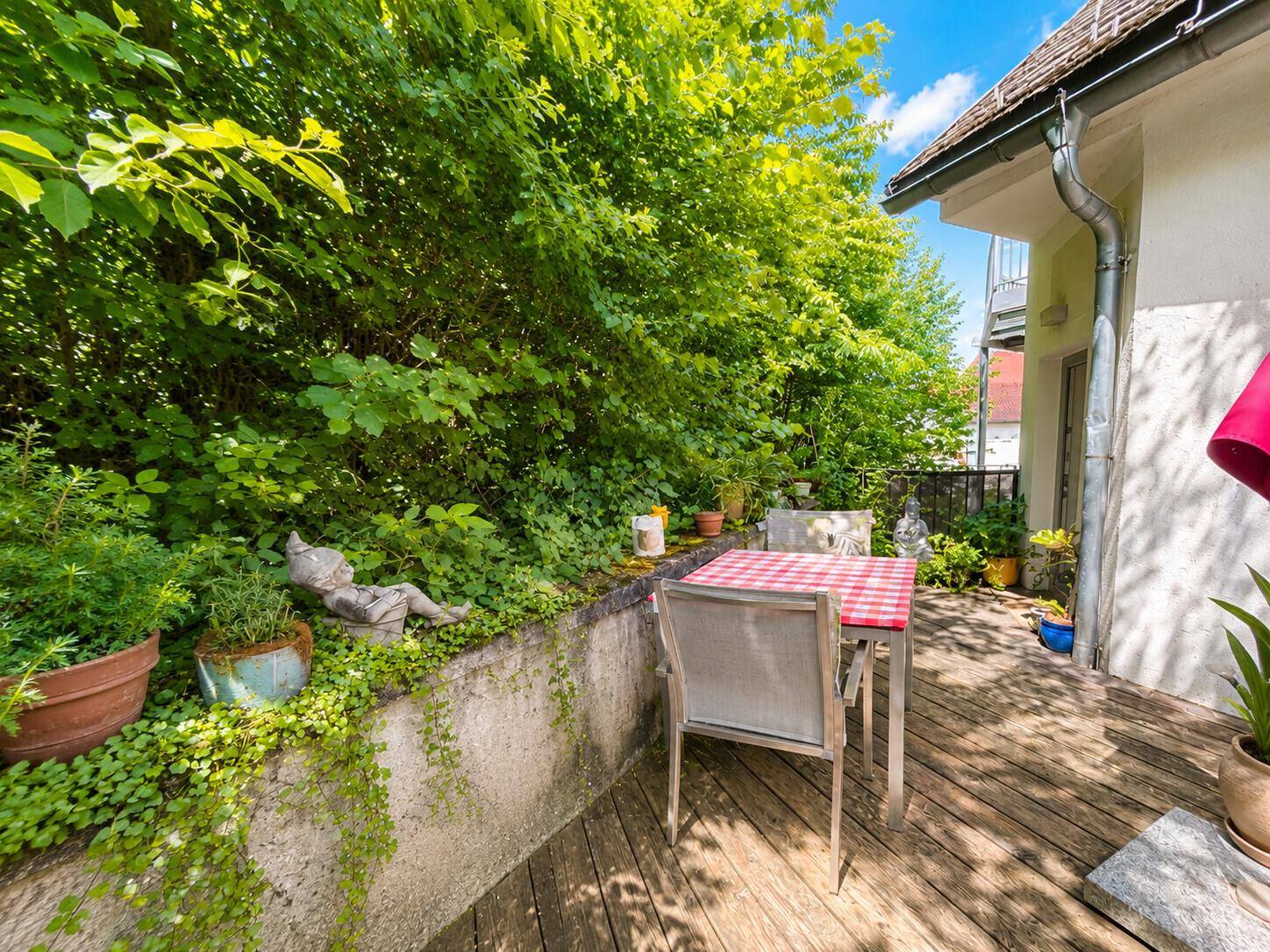 Kleine, gemütliche Terrasse mit Gartentisch und Stühlen, umgeben von üppigem Grün.