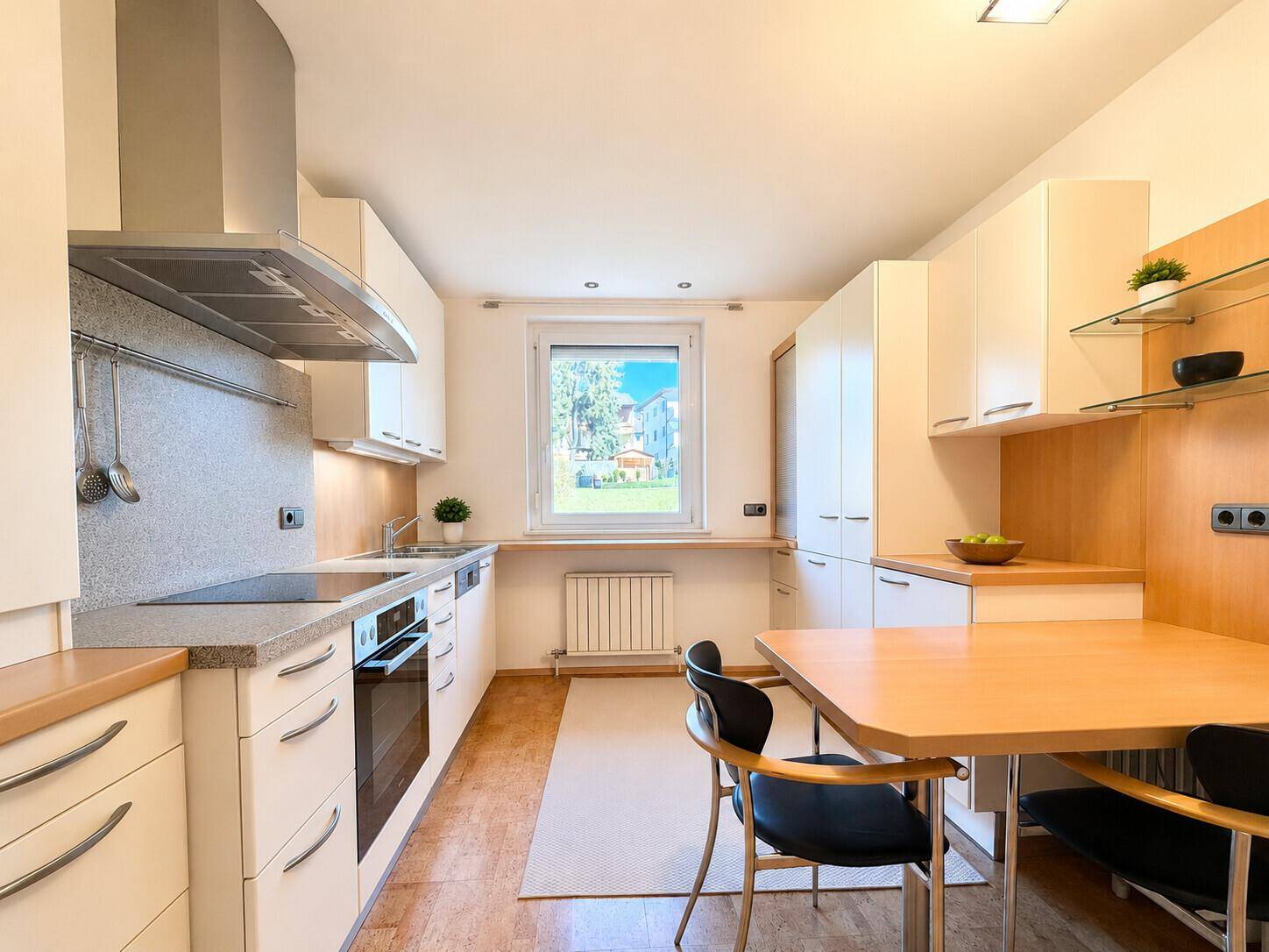 Moderne Küche mit weißen Schränken, Essbereich und Fenster mit Blick ins Grüne.