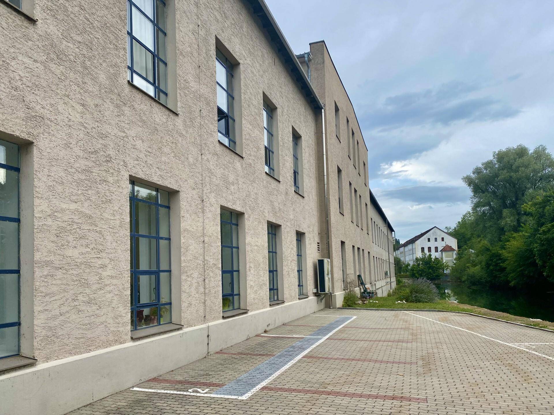 Seitenansicht eines Gewerbegebäudes mit Parkplätzen und großen Fenstern unter bewölktem Himmel.