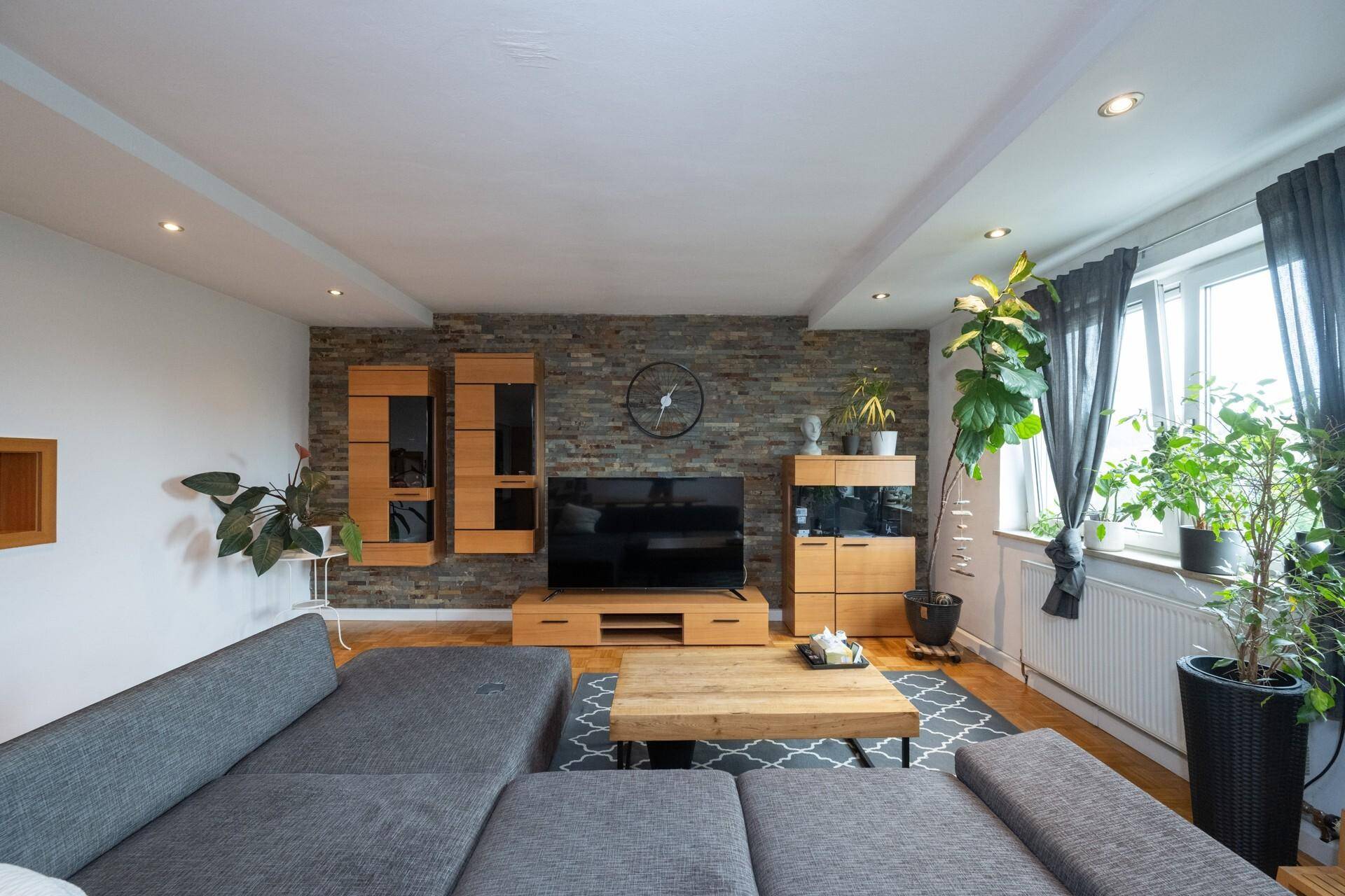 Wohnzimmer mit dekorativer Steinwand, TV-Bereich und modernen Holzmöbeln.