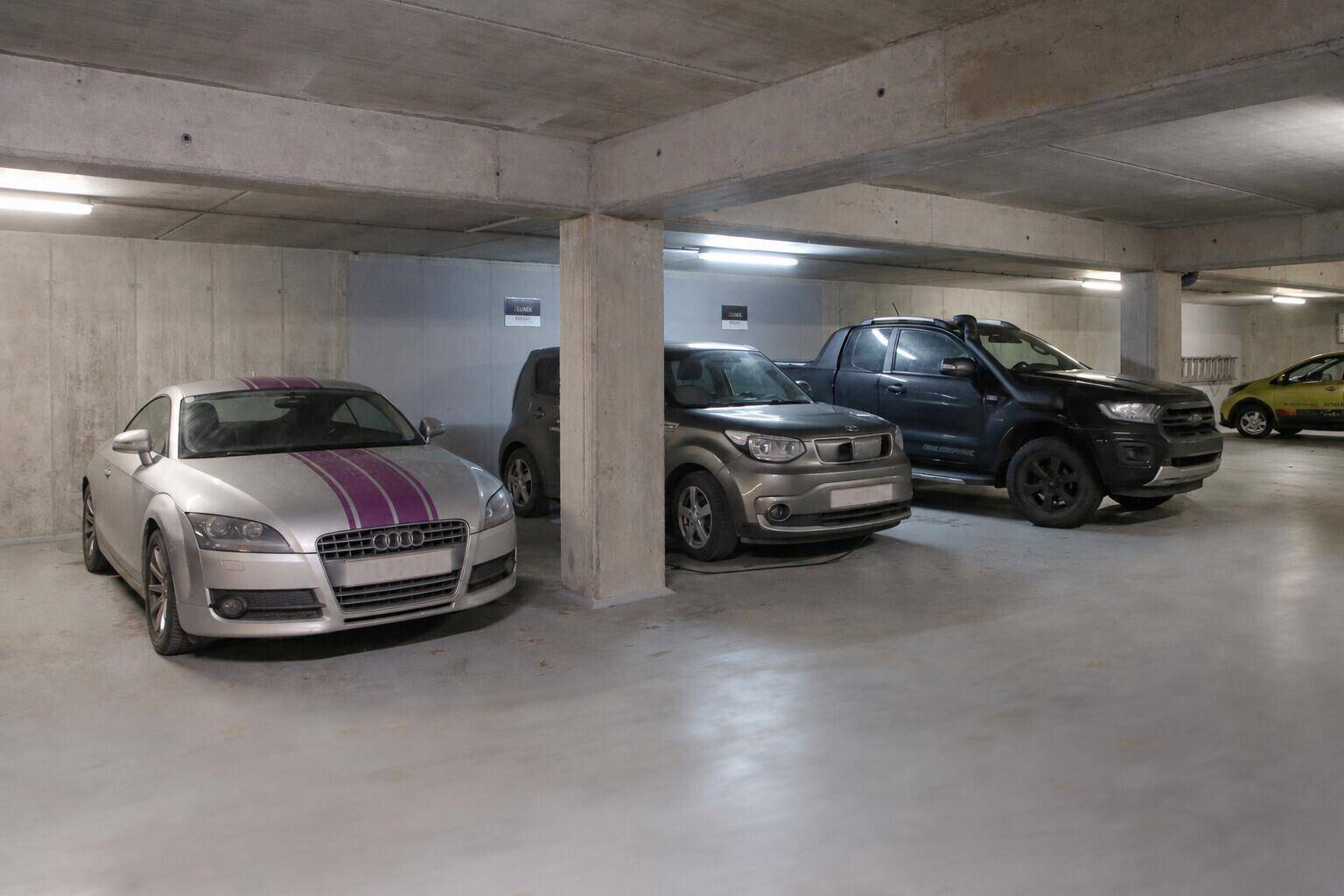 Helle Tiefgarage mit sauberem Betonboden und mehreren geparkten Fahrzeugen.