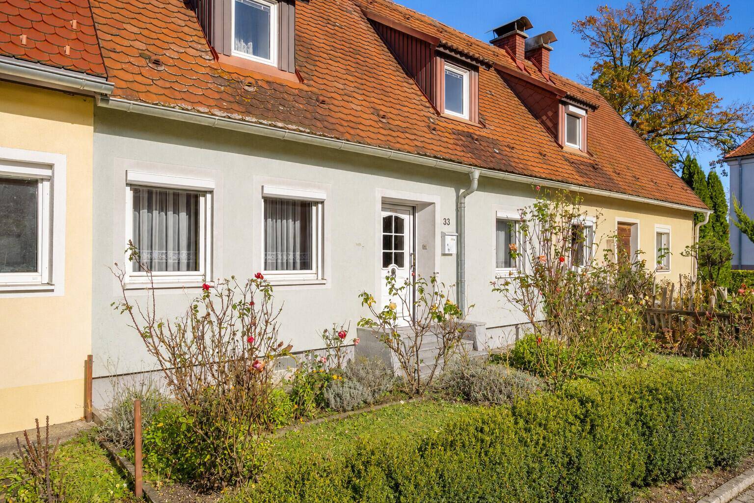 Schrägansicht eines Reihenhauses mit Vorgarten und blühenden Sträuchern.