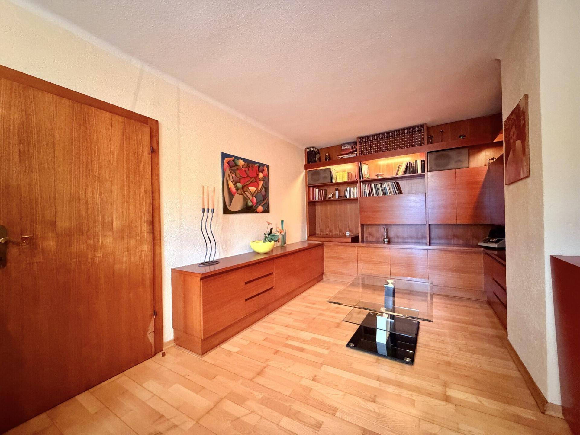 Wohnzimmer mit Holzboden, Einbauregalen und einem modernen Glastisch.