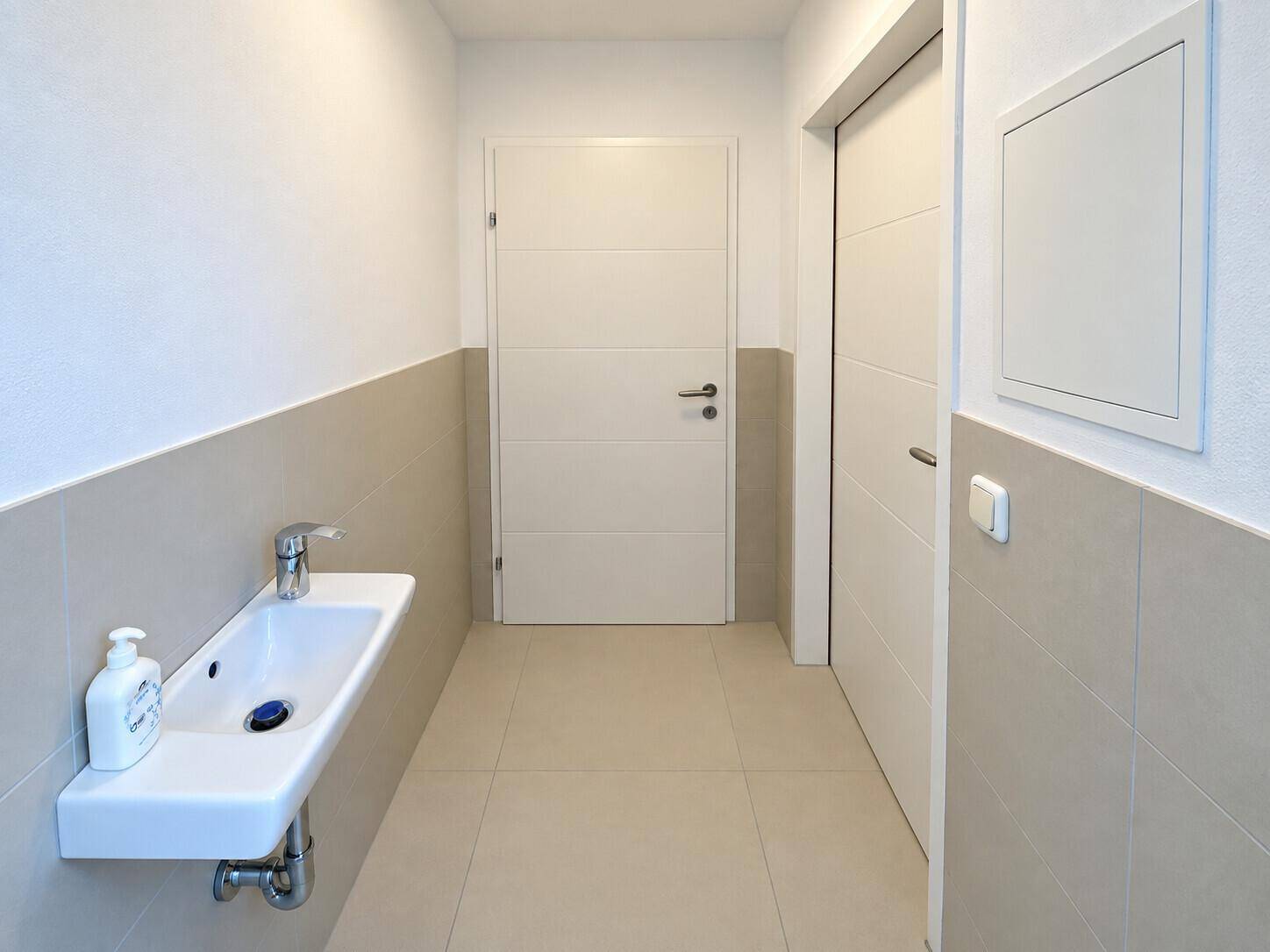 Modernes Gäste-WC mit Wandwaschbecken und hellen Fliesen, in einem gepflegten Zustand.