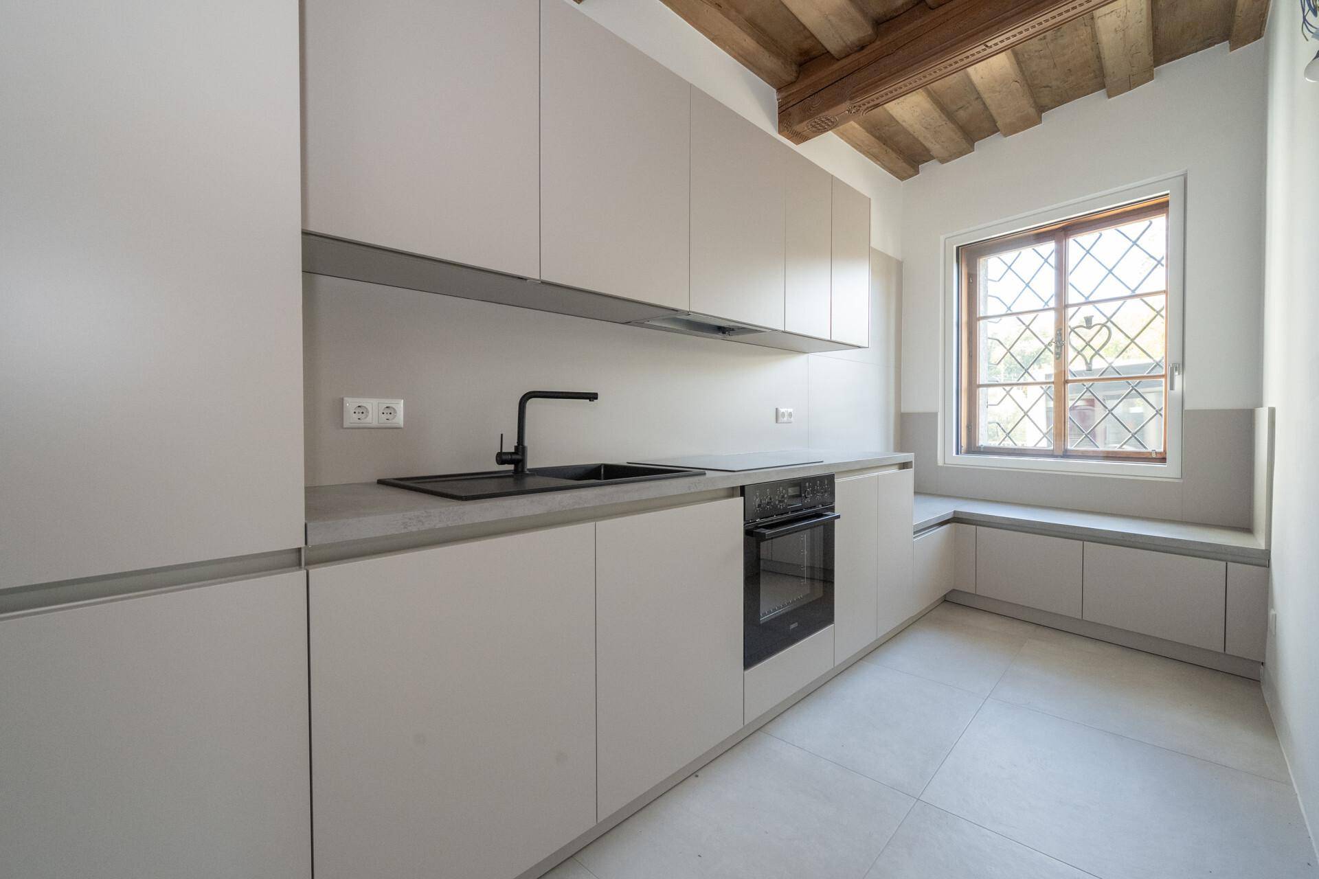 Moderne Einbauküche in hellem Grau mit integriertem Backofen und Fensterbank-Sitzgelegenheit.