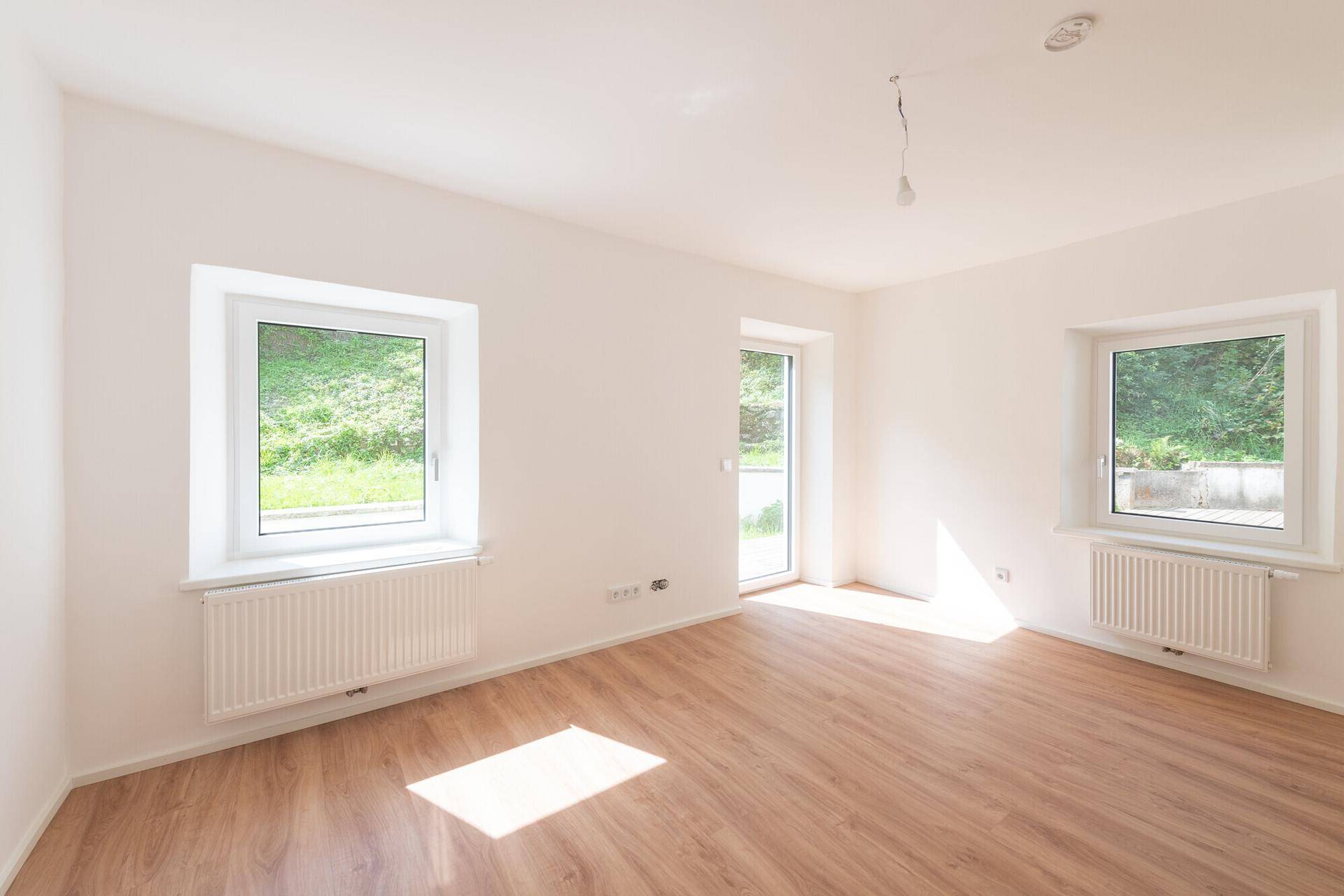 Lichtdurchfluteter Raum mit Laminatboden und Zugang zur Terrasse, ideal für Wohnzwecke.