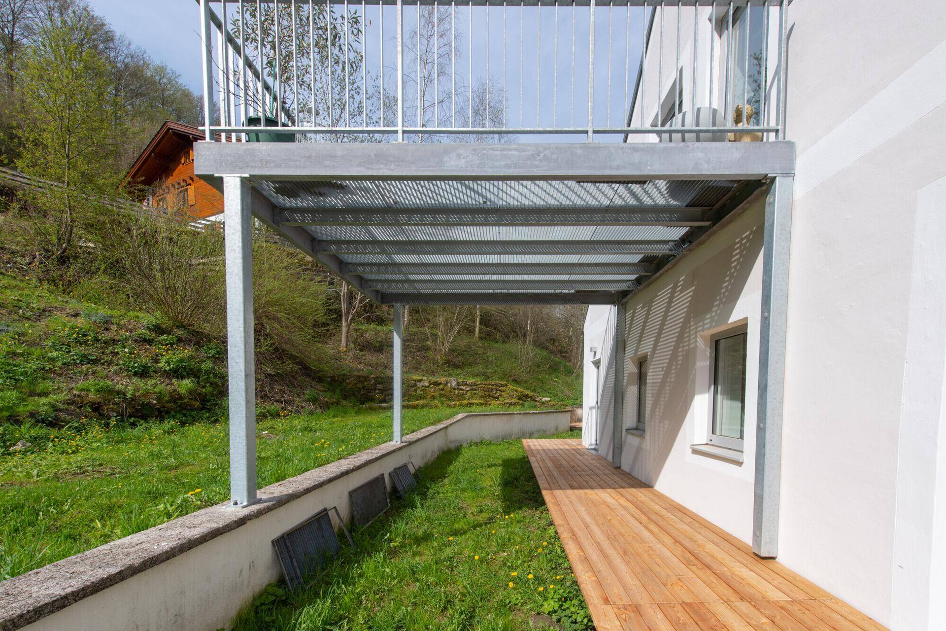 Überdachte Holzterrasse unter dem Balkon mit Blick auf die grüne Umgebung.