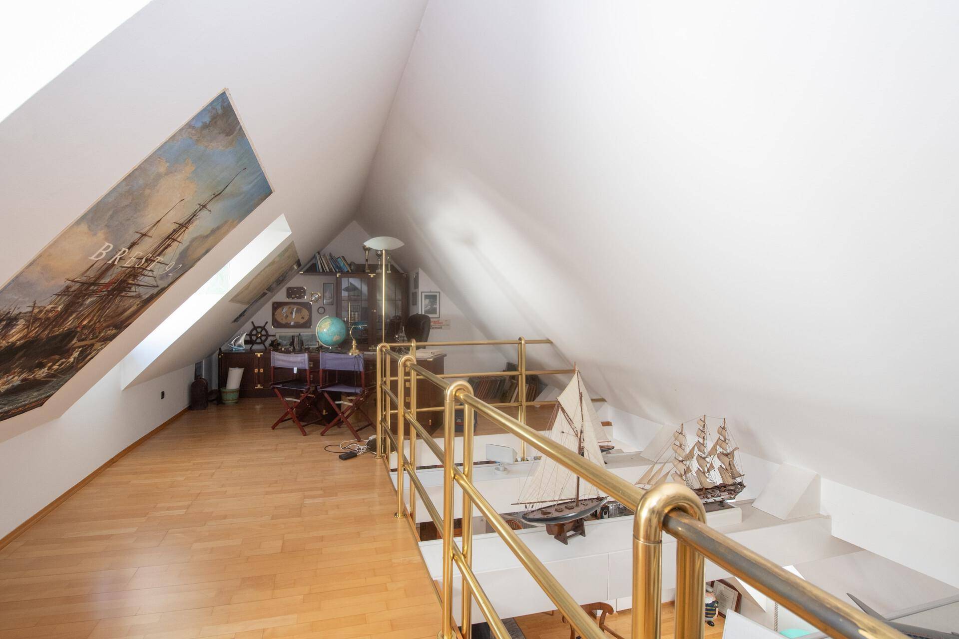 Helle Galerie im Dachgeschoss mit Holzfußboden, Schiffsmodellen und schrägen Wänden.