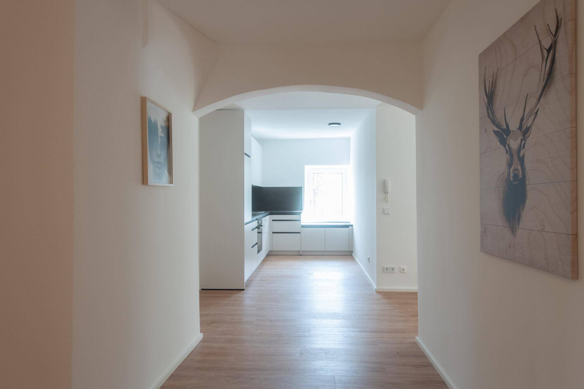 Heller Flur mit Holzboden und einem Bogen, der in die moderne Küche führt.