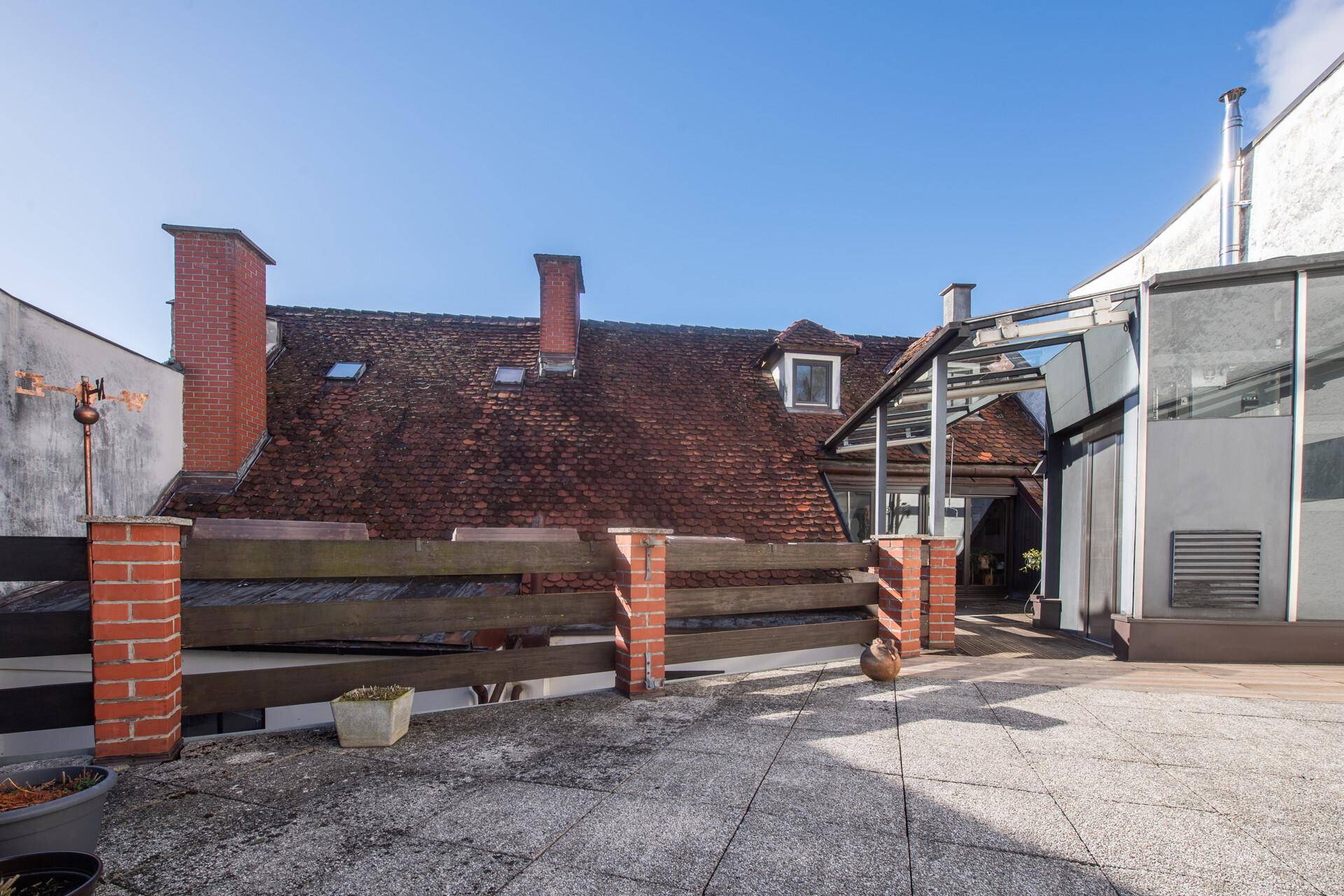 Sonnige Dachterrasse mit Blick auf historische Ziegeldächer und Schornsteine.